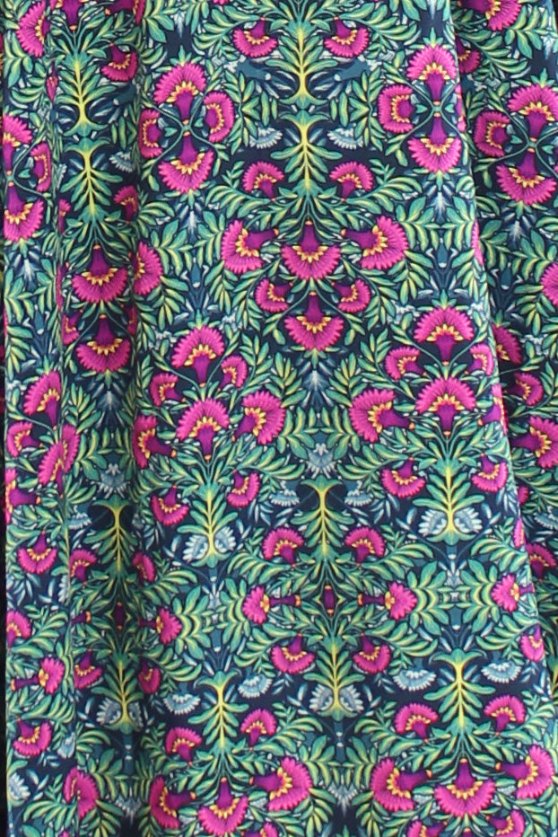 Detailansicht vom Stoff eines geblümten Sommerkleids in Grün, mit auffälligem floralen Muster in Pink und Gelb auf dunkelgrünem Hintergrund.