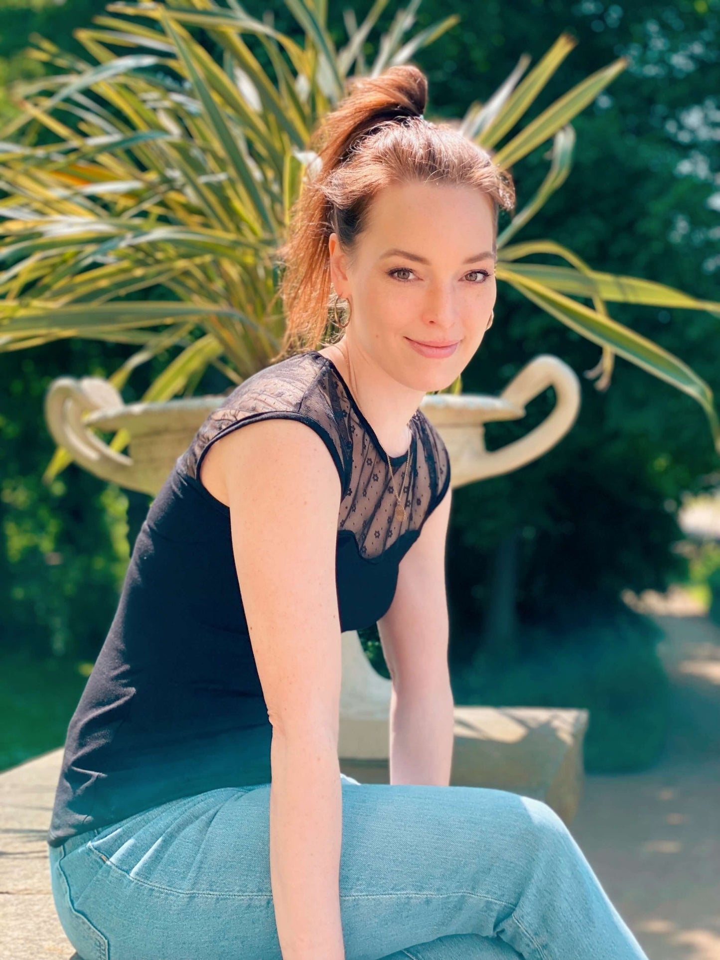 Frau in einem eleganten, engen Top in schwarz mit Blumentüll von LA.LUKA Berlin, sitzt auf einer Mauer.