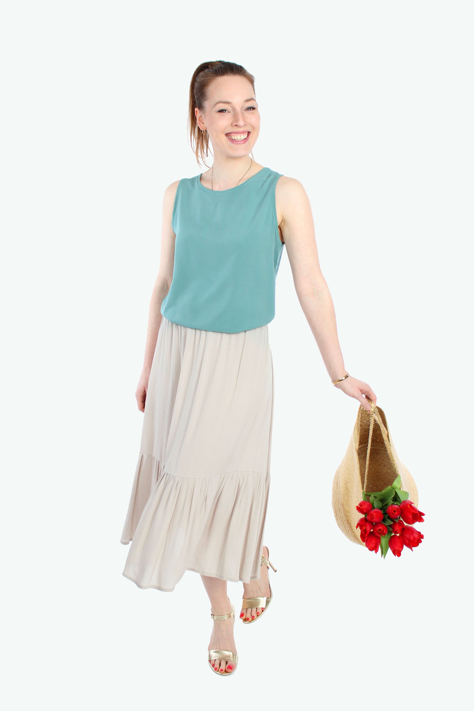 Frau, in einem sommerlichen Midirock aus leichtem Viskose Crepe in hellen beige mit Volant und elastischen Bund, in der Hand trägt sie eine Tasche mit Blumen.