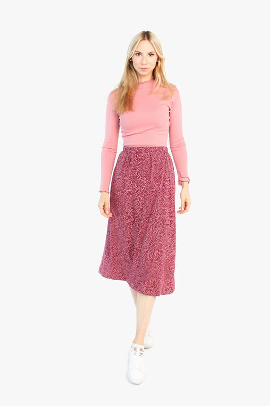 Model in einem Midirock in bordeaux/rosé aus Viskose und einem Rollkragenshirt aus Baumwolle in rosé von LA.LUKA Berlin.
