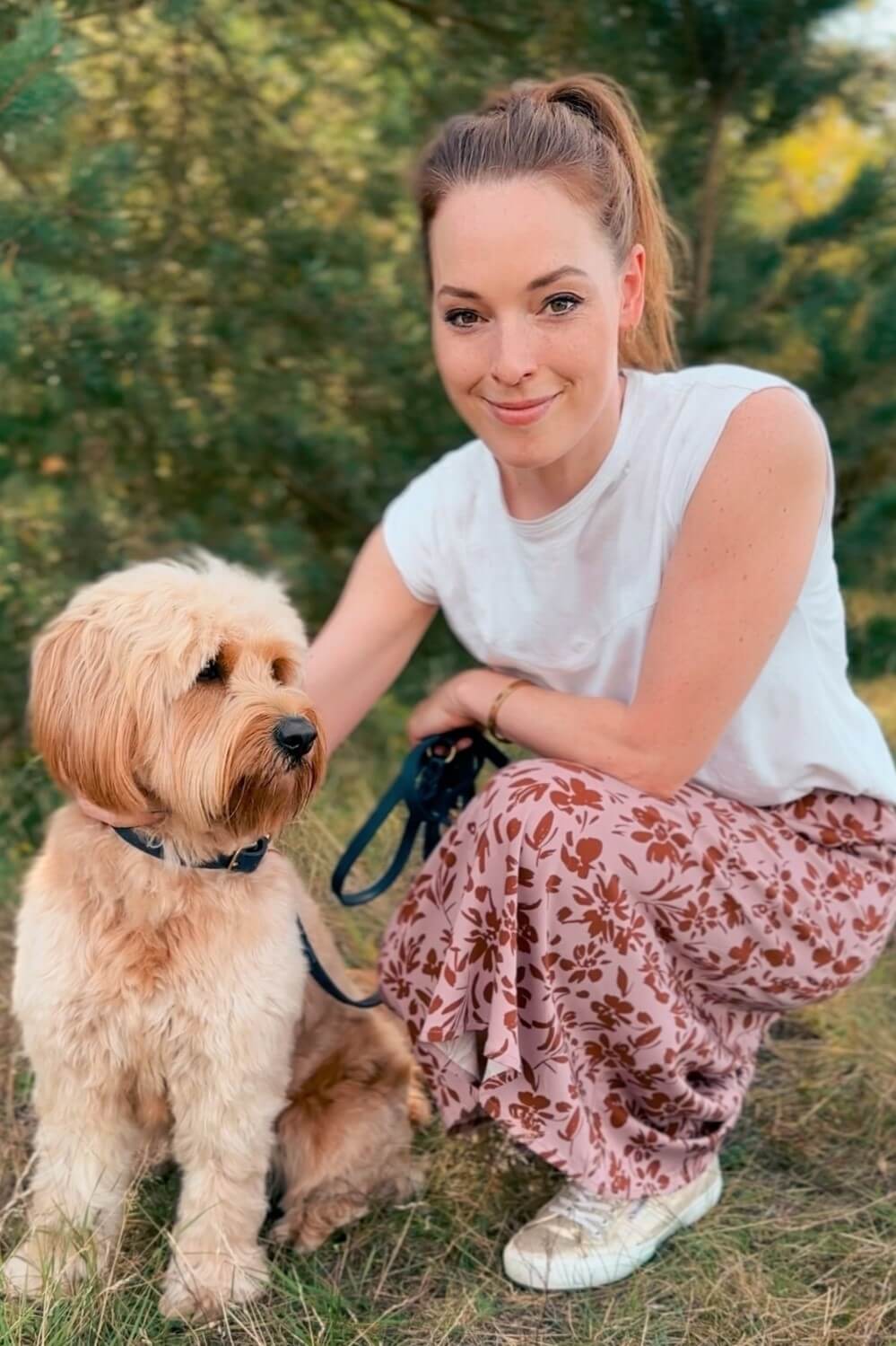 Frau mit Hund im Wald. Die Frau trägt einen Midirock mit Blumenprint in rosé und braun. - LA.LUKA Berlin