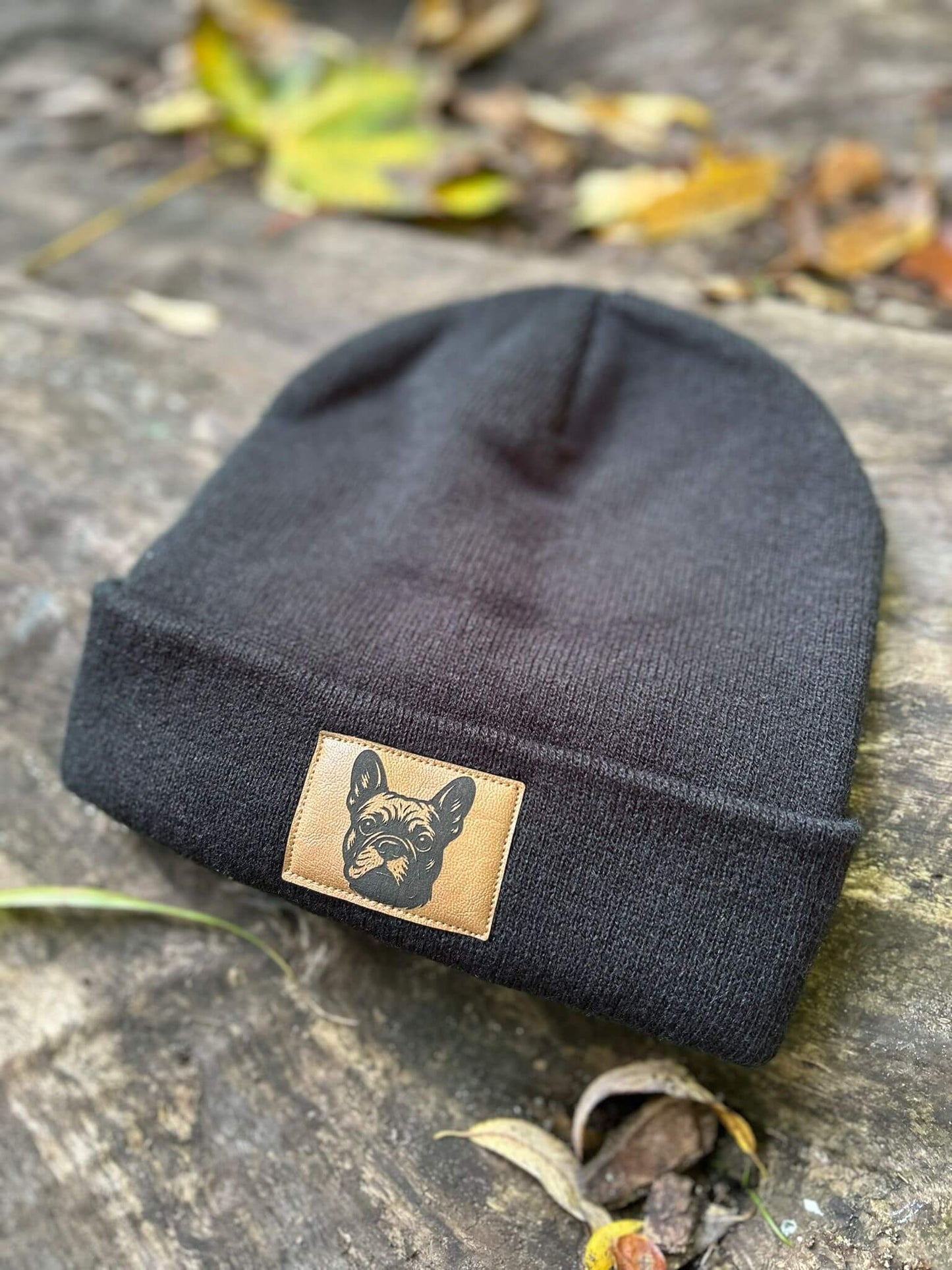 Schwarze Mütze von LA.LUKA Berlin mit braunem Kunstlederpatch und Aufdruck einer Französischen Bulldogge, fotografiert im herbstlichen Outdoor-Setting