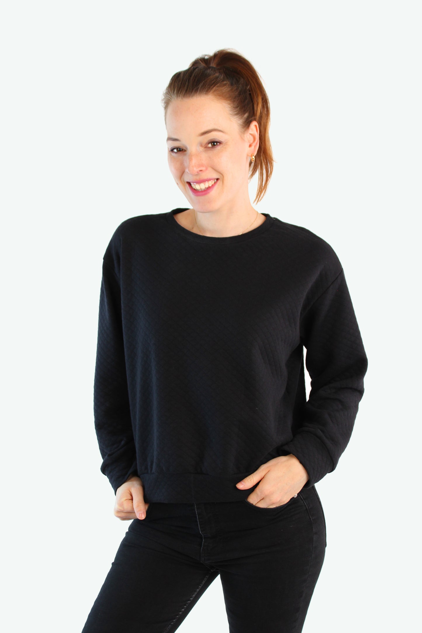 Frau trägt schwarzen Pullover mit Strukturmuster in lockerem Schnitt, steht seitlich mit den Händen in den Taschen – LA.LUKA Berlin Herbstkollektion.