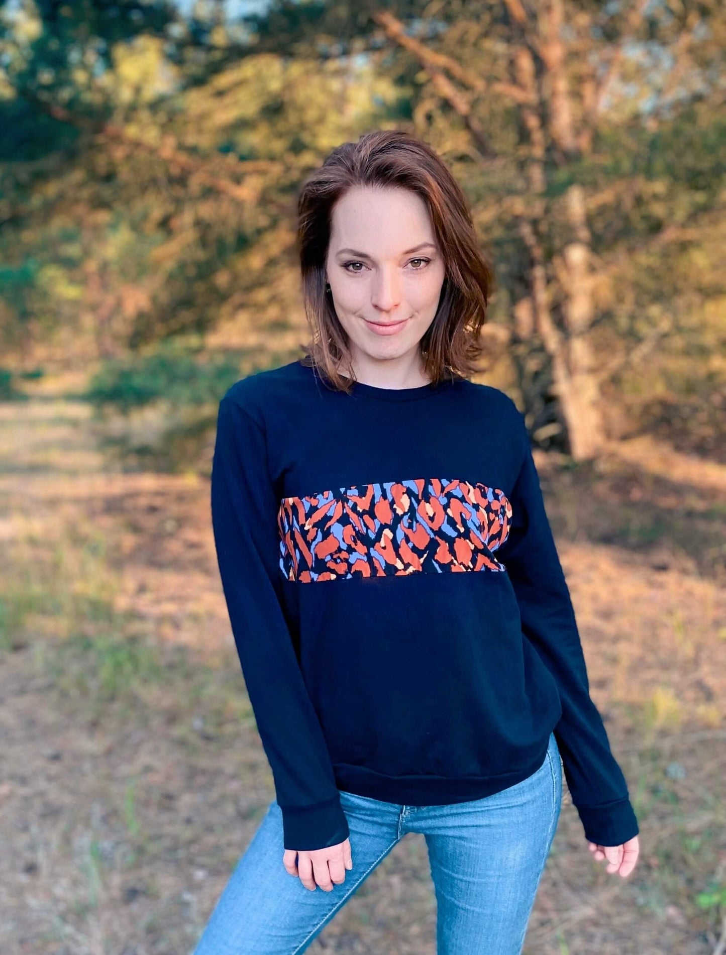 Frau in einem schwarzen Pullover von LA.LUKA Berlin, die in einer Waldlichtung steht.