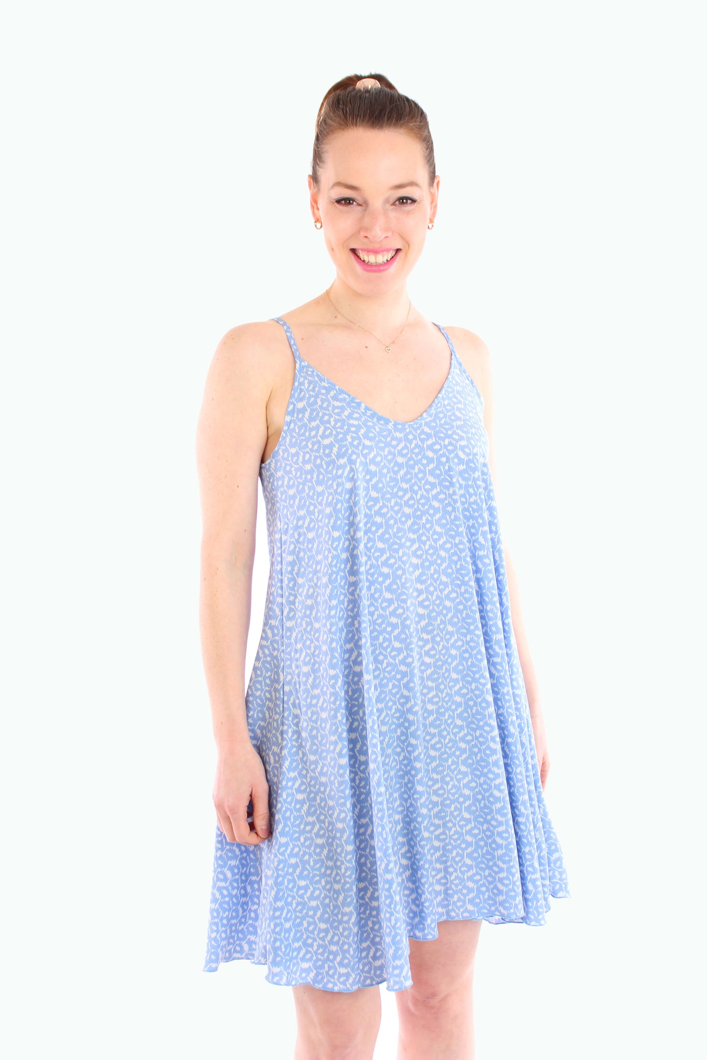 Frau trägt ein luftiges, blau gemustertes Minikleid mit Spaghettiträgern und V-Ausschnitt – perfekt als Sommer- oder Strandkleid.