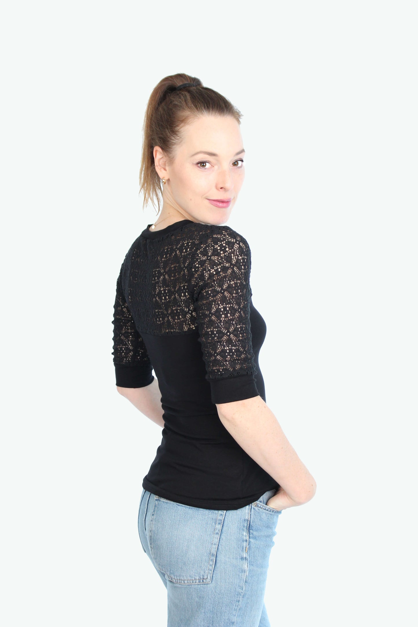 Frau, in einem schwarzen Top mit Spitzenärmel, schaut seitlich über die Schulzer.