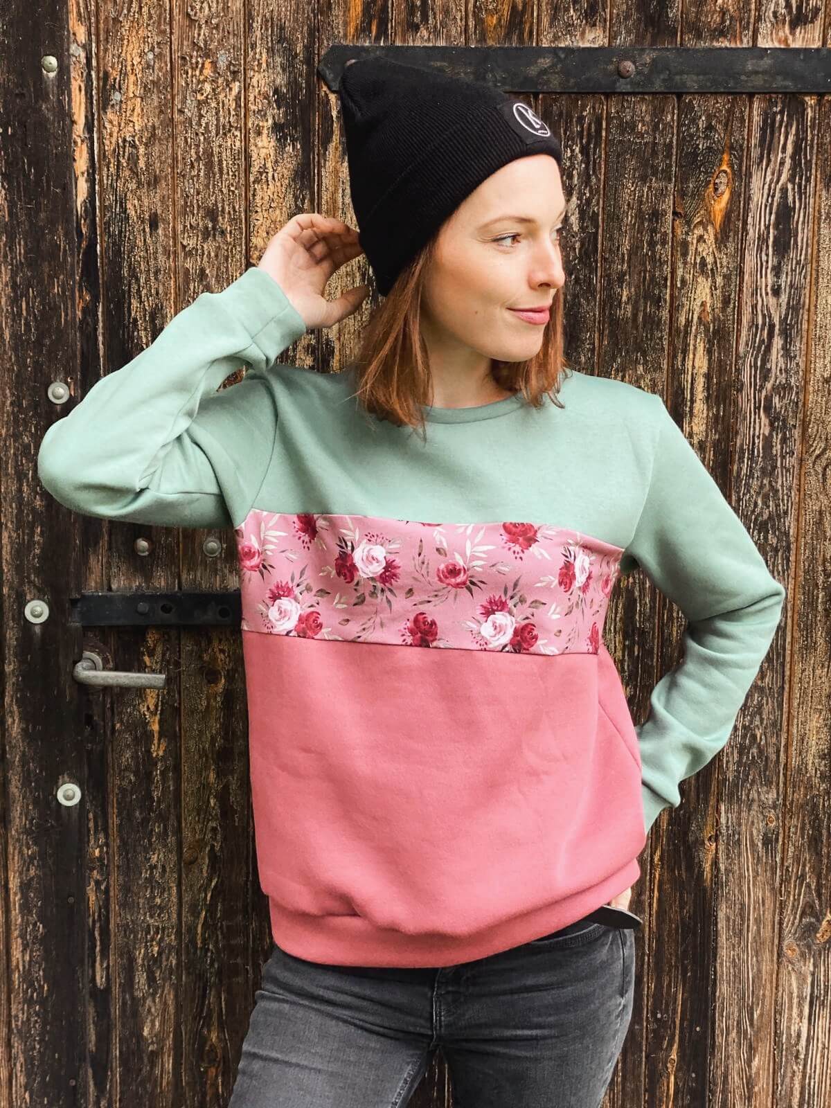 Frau, trägt einen Pullover aus Baumwolle in mint und rosé mit Blumenprint dazu eine schwarze Mütze mit dem Logo von LA.LUKA Berlin.
