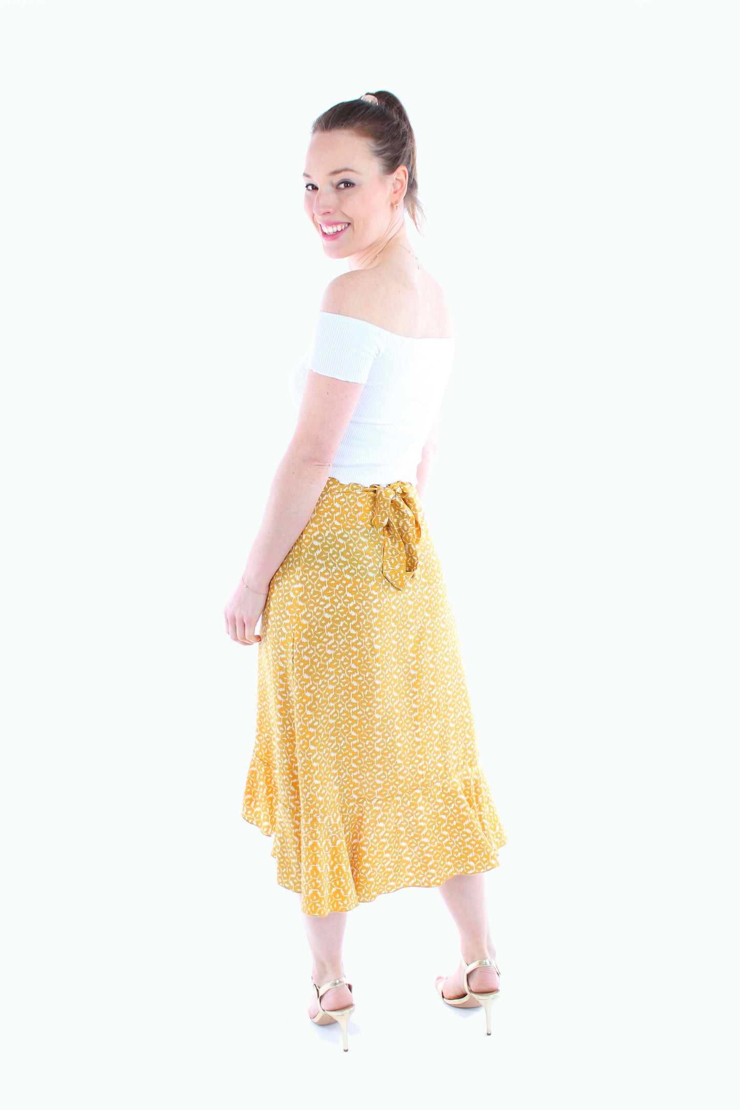 Rückansicht eines gelb-weißen Sommerrocks in Wickeloptik. Der luftige Midirock aus Viskose hat einen Volant-Saum und wird an der Taille gebunden.