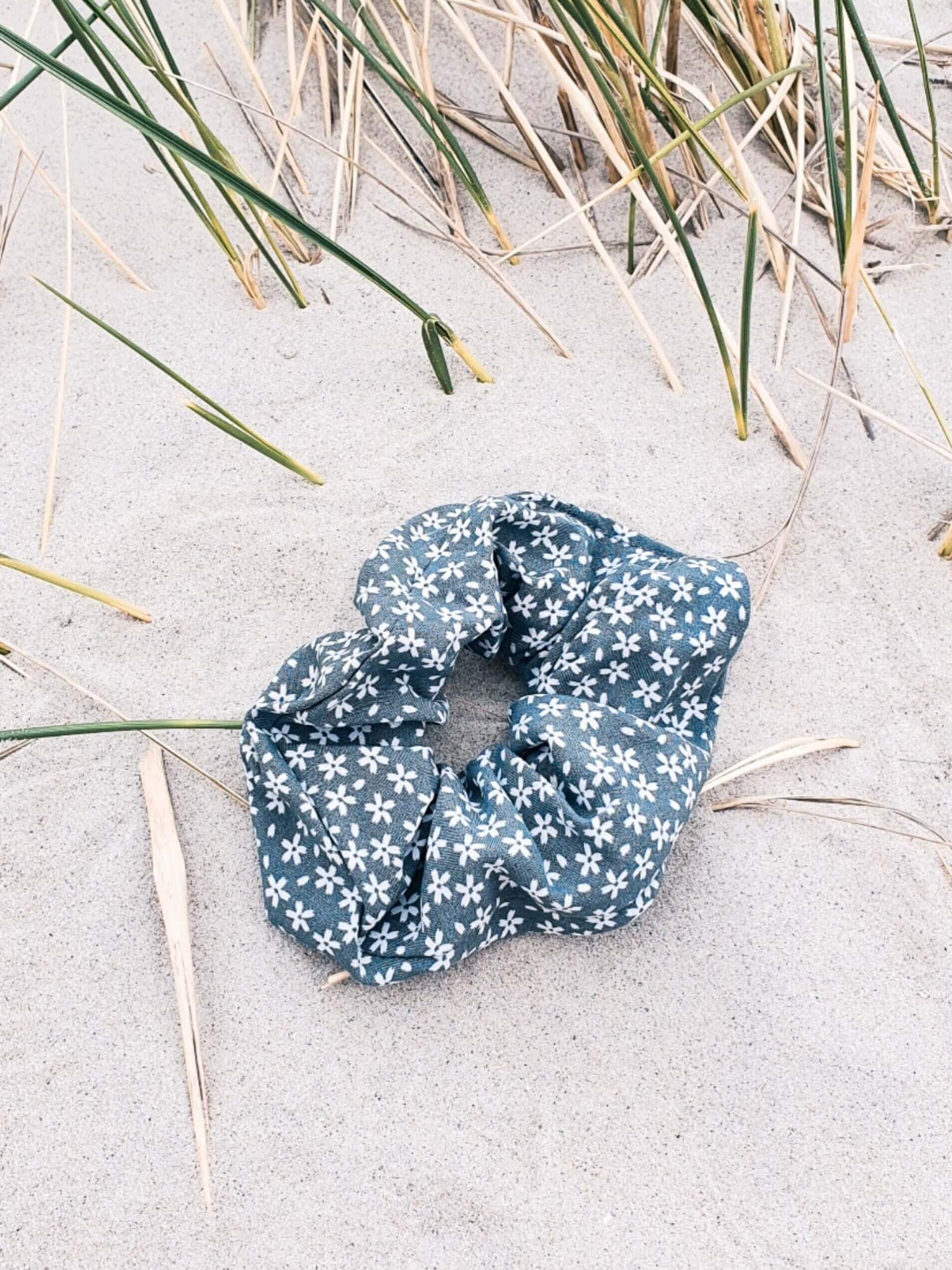 Scrunchie in grün mit weißen Blümchen, liegt im Sand.