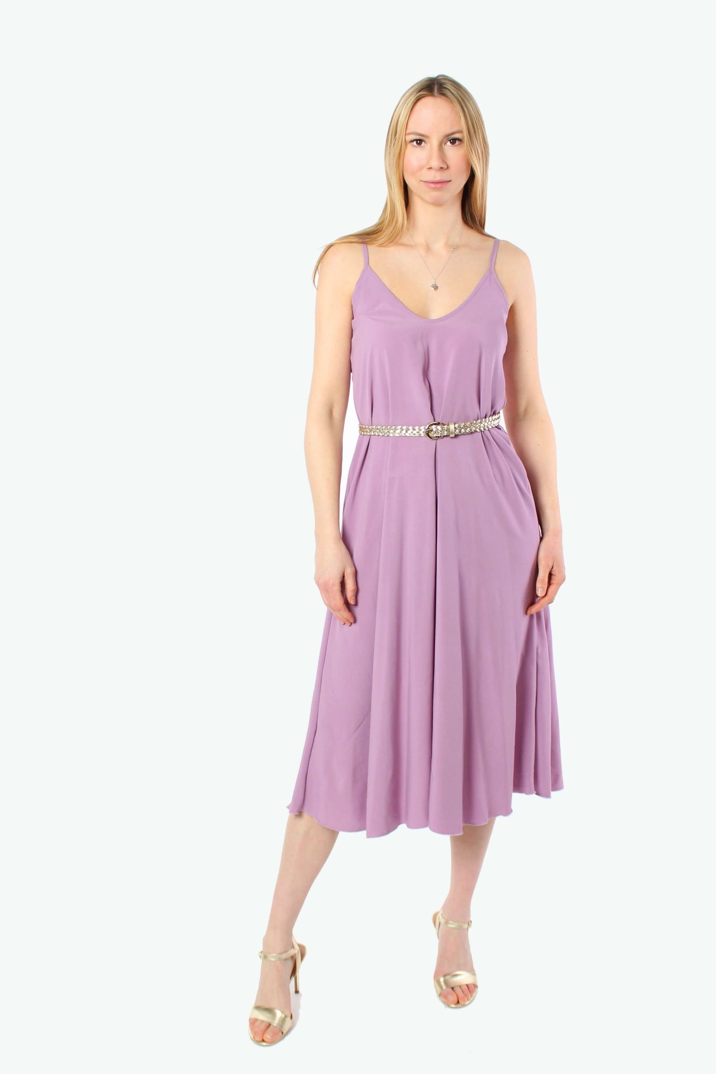 Blondes Model trägt ein fliederfarbenes Midikleid aus Viskose mit schmalem Gürtel, Spaghettiträgern und goldenen Absatzsandalen.