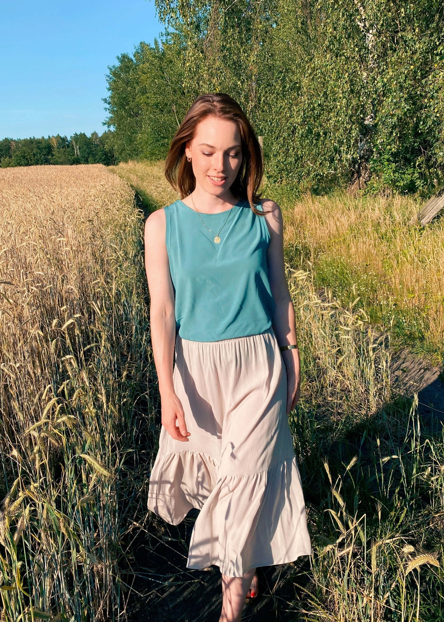 Frau in einem sandfarbenen Sommerrock in Midilänge mit Voalnt von LA.LUKA Berlin auf einem Feld.