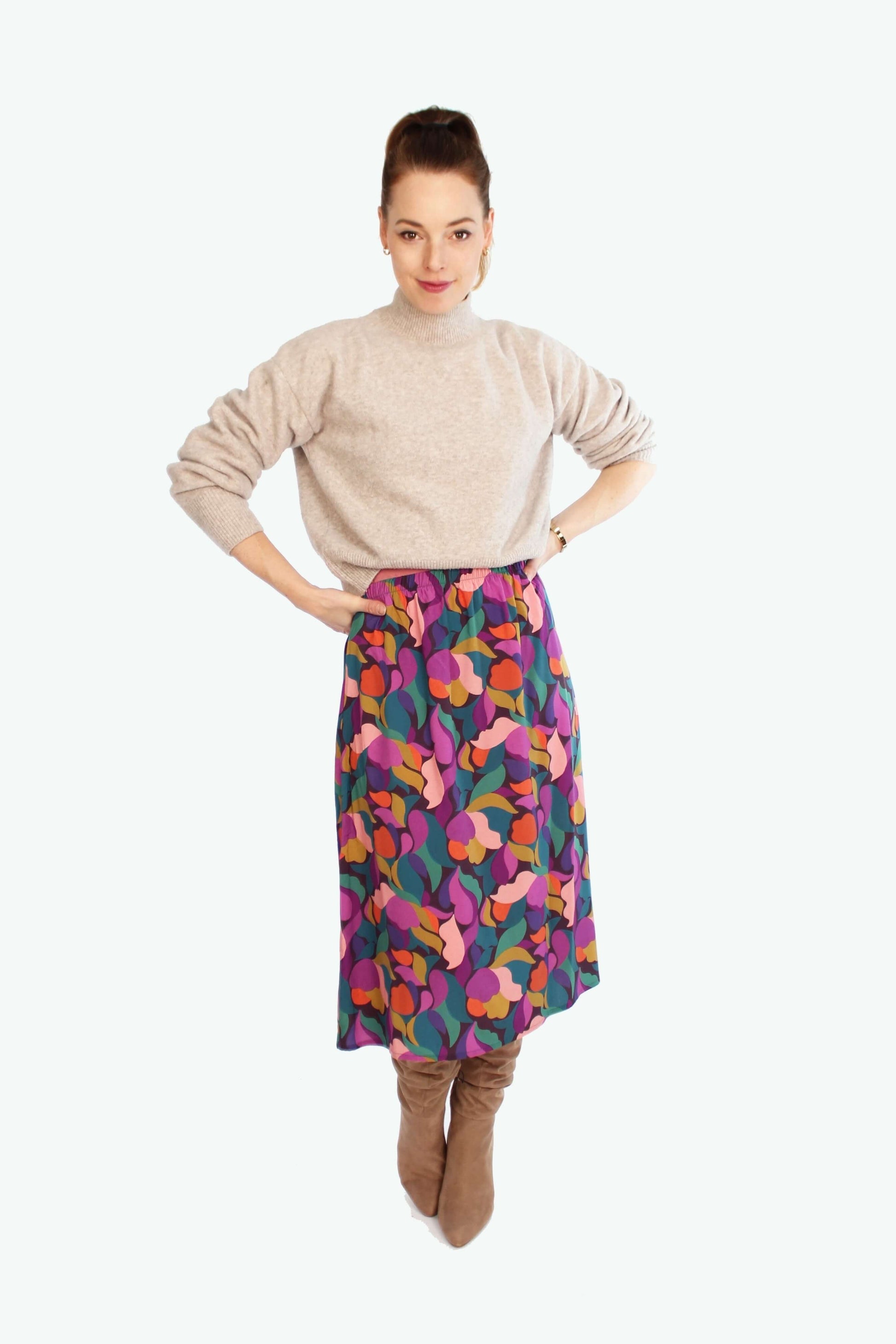 Midirock mit lebendigem Allover-Muster in Pink, Orange und Grün von LA.LUKA Berlin – herbstlich gestylt mit beigem Strickpulli und kniehohen Stiefeln.