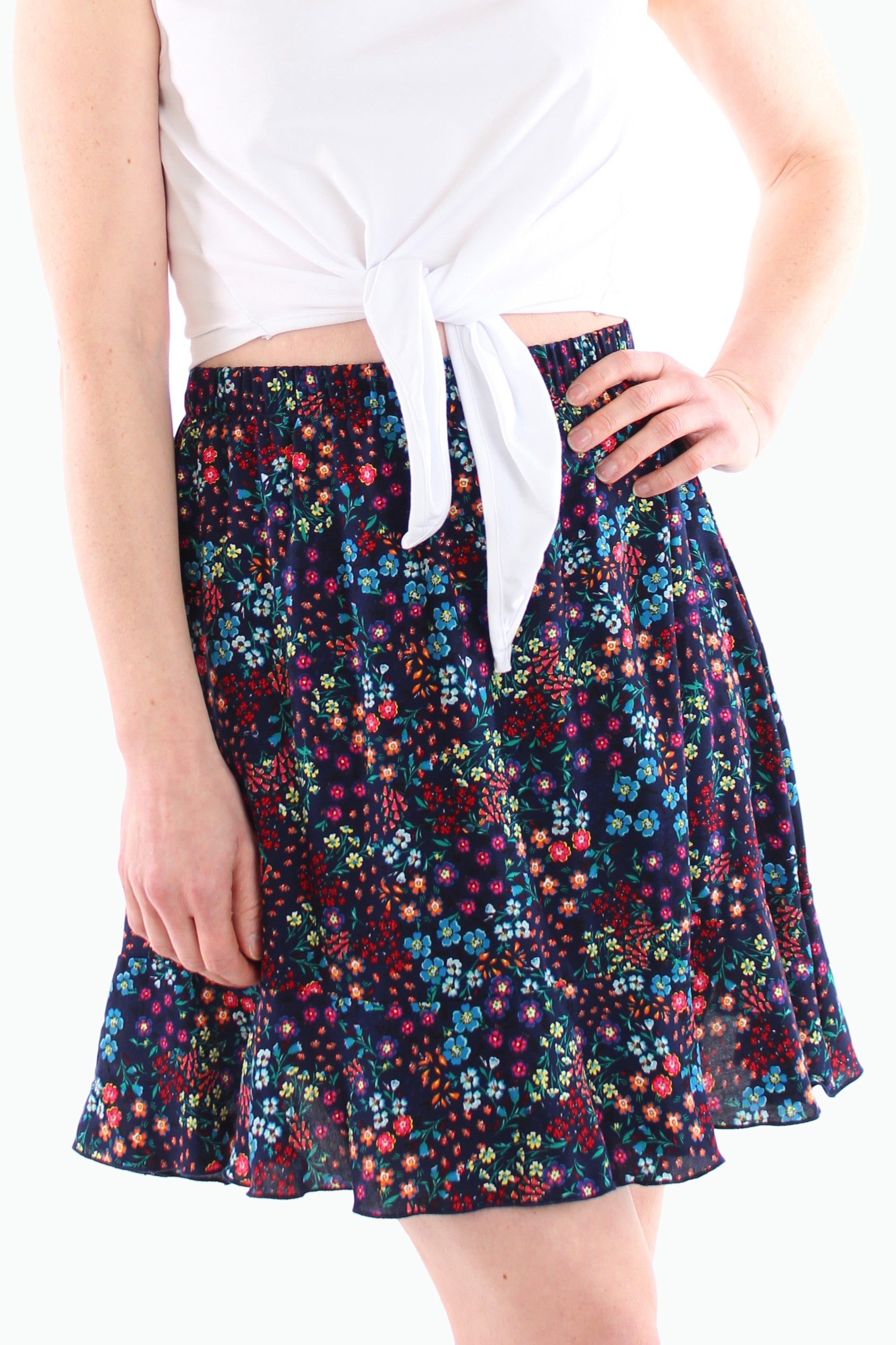 Detailaufnahme eines dunkelblauen Minirocks mit buntem Blumenmuster und Volant-Saum, kombiniert mit einem weißen Knotenshirt – Sommerlook für 2025.