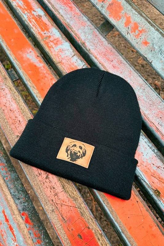 Mütze mit Australian Labradoodle Motiv in schwarz von LA.LUKA Berlin, liegt auf einer Parkbank.