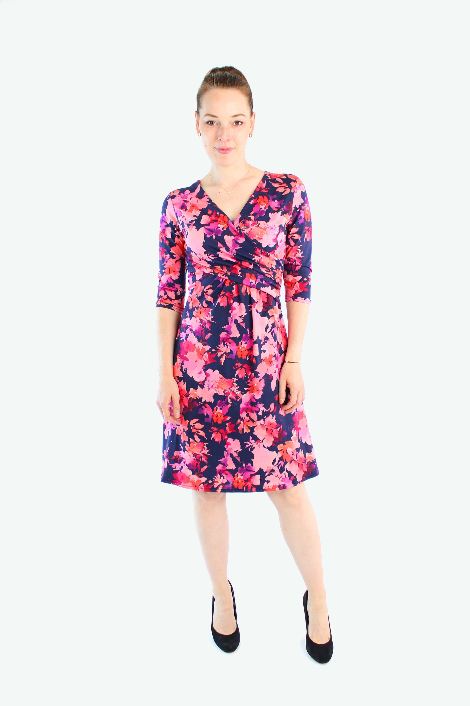 erseykleid in Dunkelblau mit pink-rotem Blumenprint, V-Ausschnitt, 3/4-Ärmeln und knieumspielender Länge, getragen mit schwarzen Pumps.