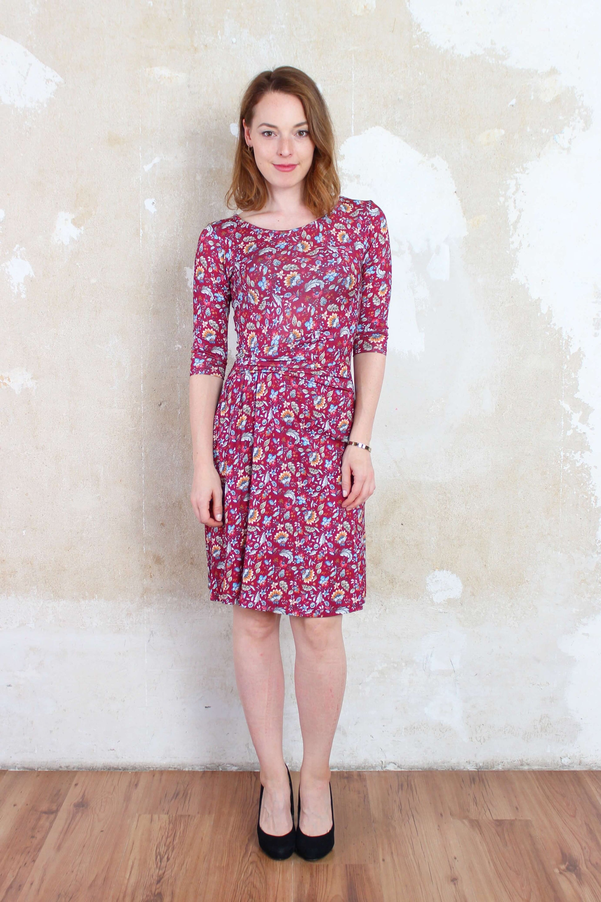 Frau in einem elegnaten, knielangen Jerseykleid in bordeauxrot mit bunten Blumenmuster von LA.LUKA Berlin.