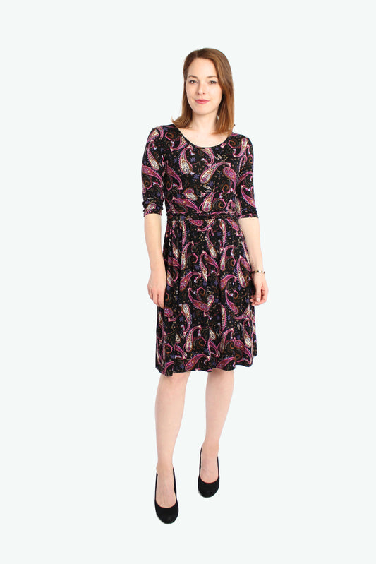 Frau in einem knielangen, schwarzen Jerseykleid mit lila Paisleymuster und Rundhalsausschnitt von LA.LUKA Berlin.