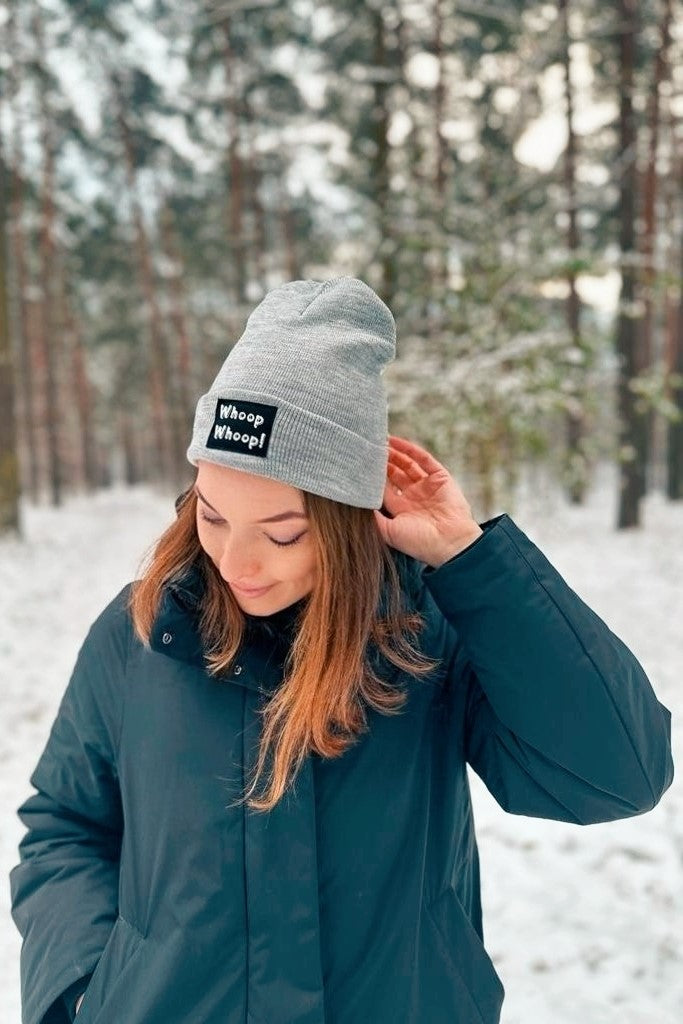 Frau trägt eine graue Mütze mit Whoop Whoop! Aufnäher von LA.LUKA Berlin, im Hintergrund Wald.