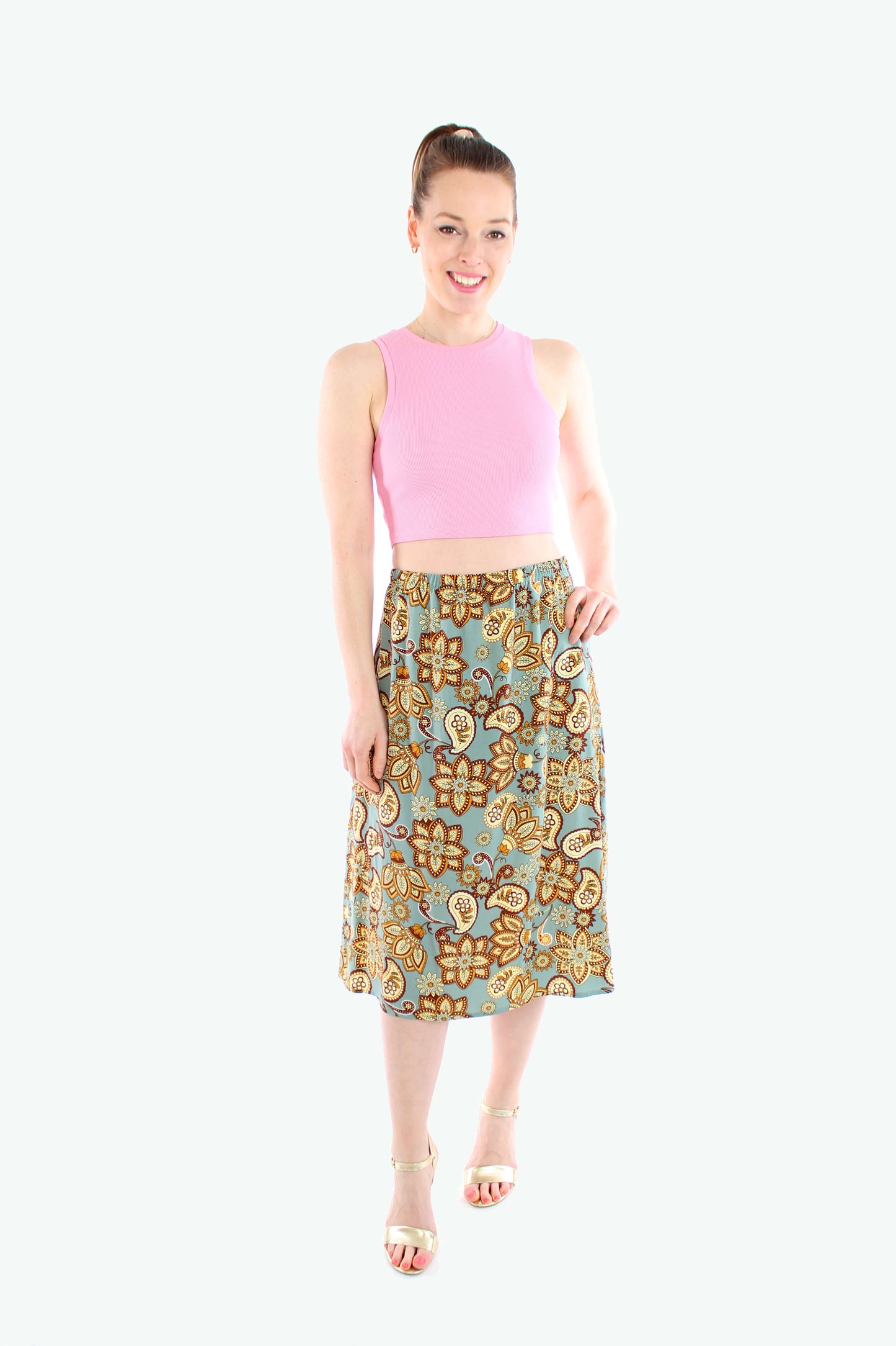 Midirock mit Paisley-Muster in Mintgrün, getragen von einem Model mit pinkem Crop-Top und goldenen Sandalen.