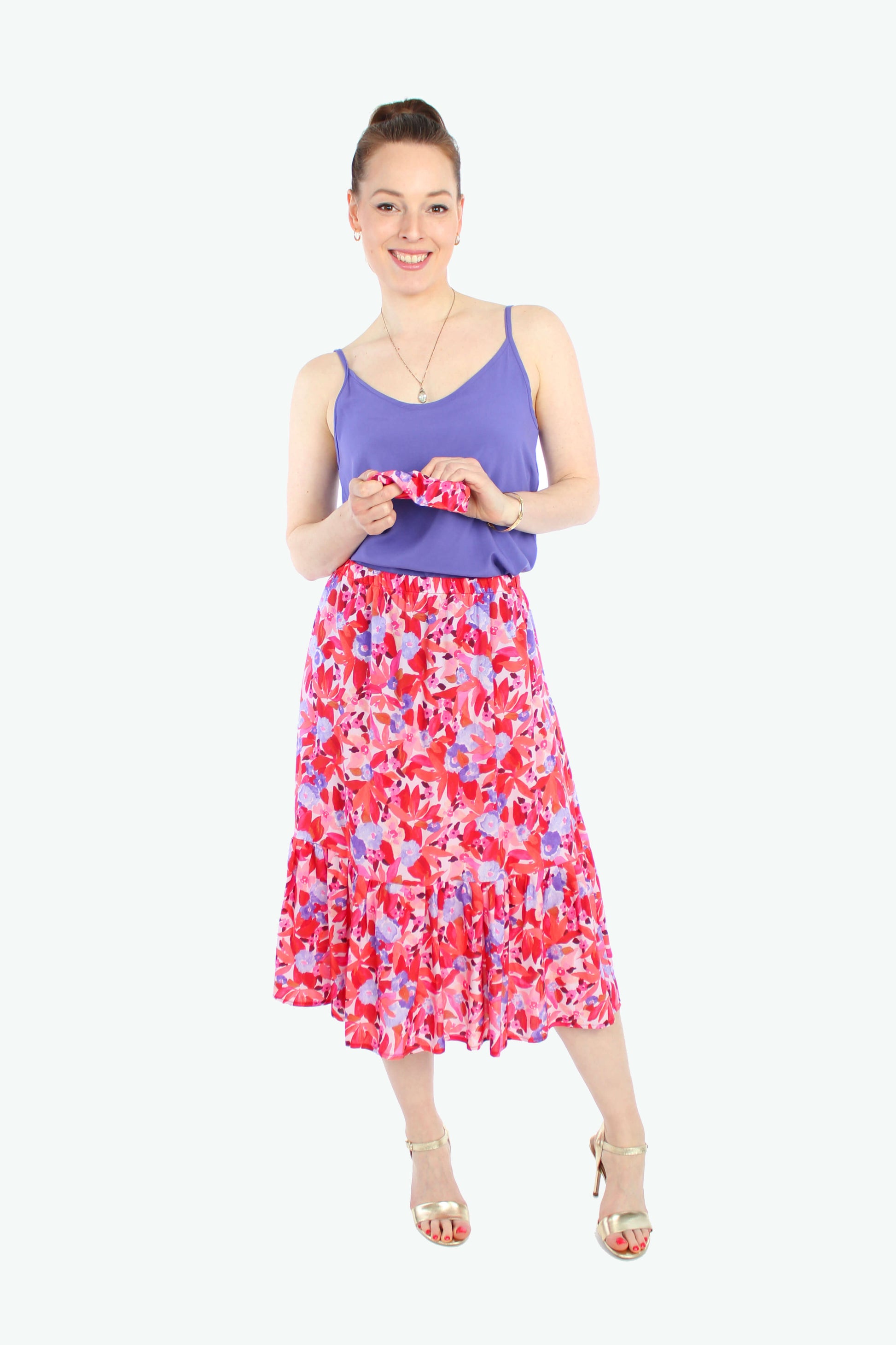 Frau, in einem sommerlichen Midirock mit Volant in rot, rosé, flieder geblümt aus leichtem Viskosestoff, dazu trägt sie ein Top mit Spaghettiträgern in lila.