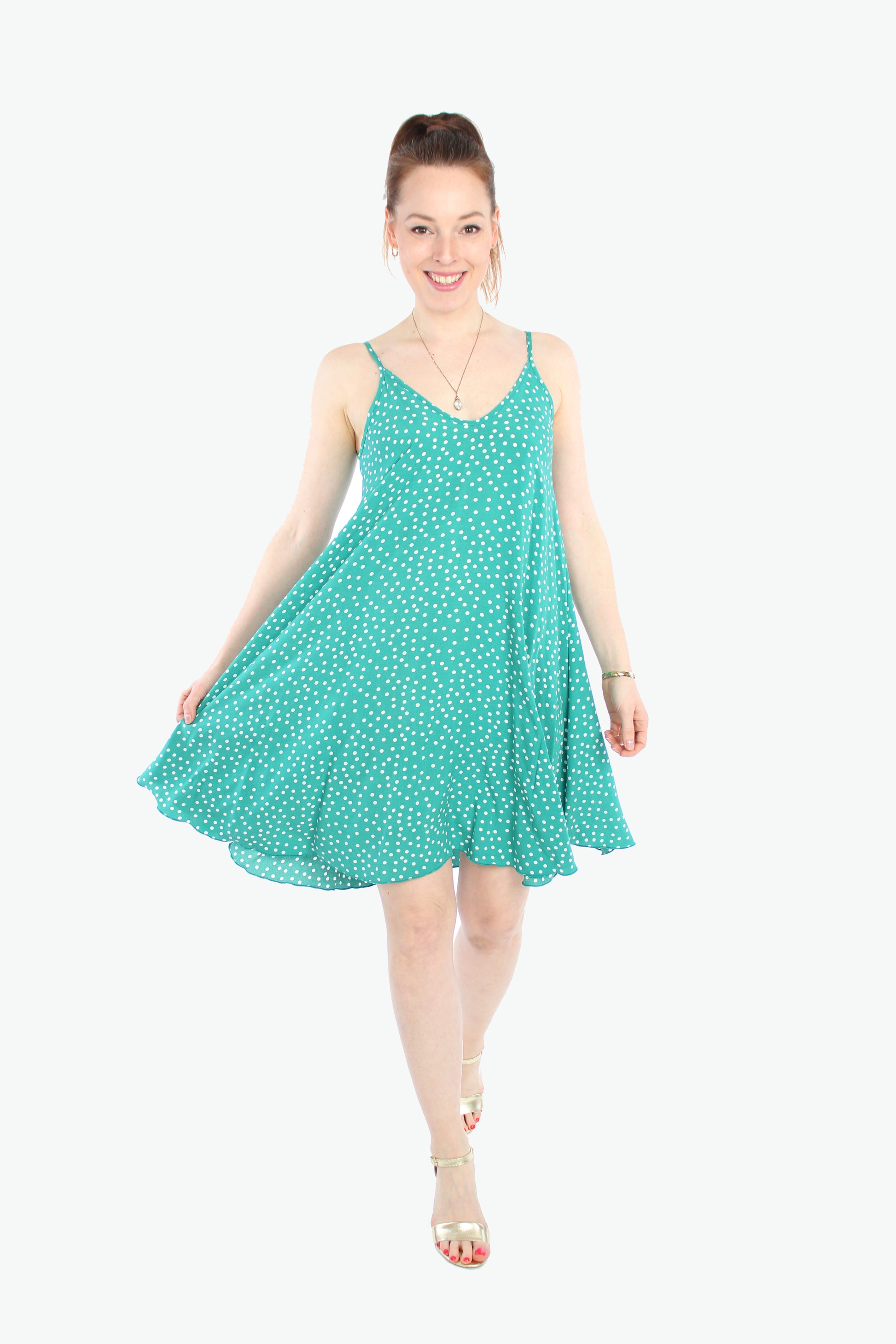 Lächelnde Frau in einem grünen Sommerkleid mit weißen Punkten. Das Kleid ist ein luftiges Trägerkleid aus 100% Viskose, kurz und perfekt für warme Tage von LA.LUKA Berlin.