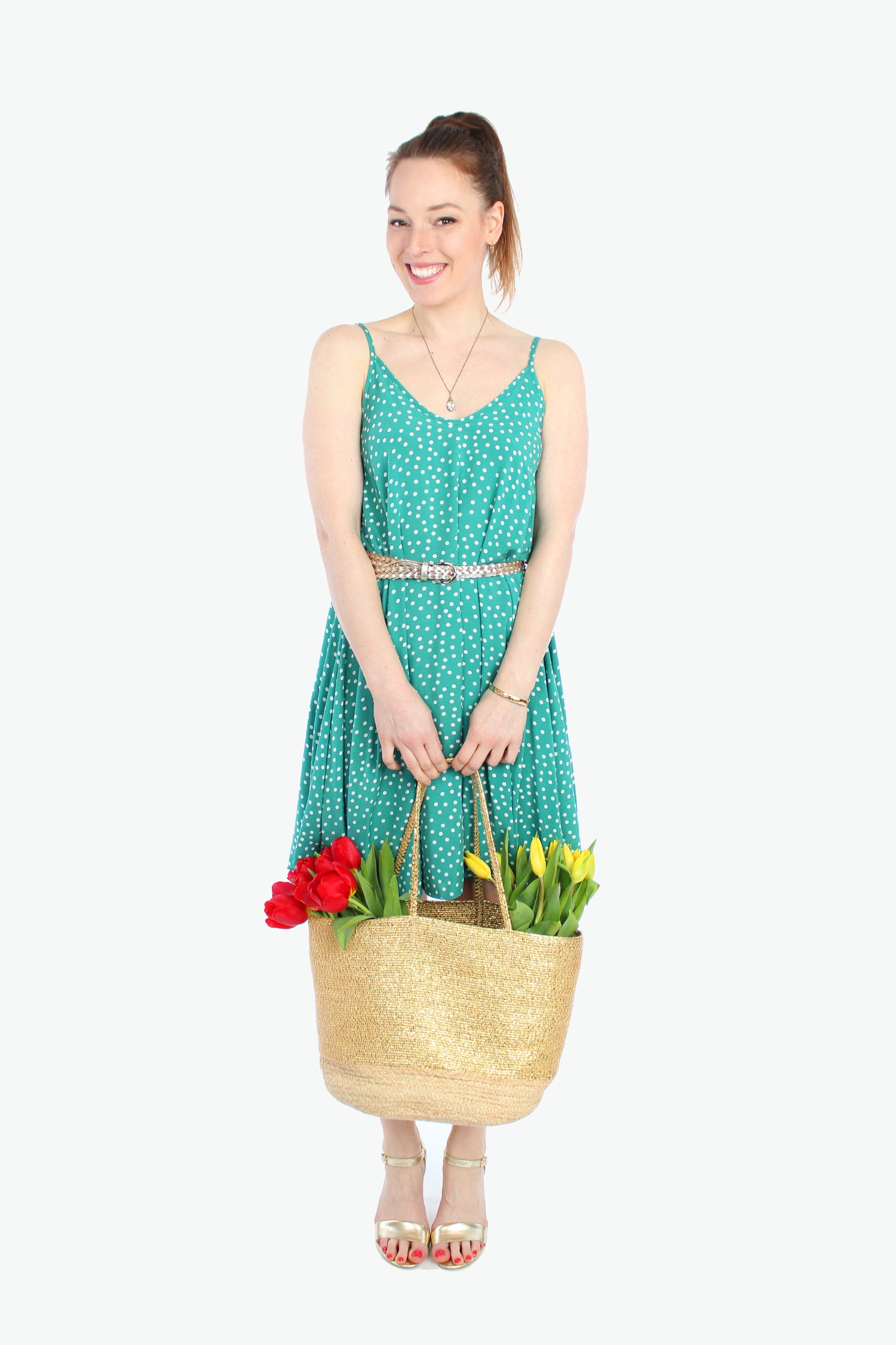 Frau, in einem sommerlichen Minikleid mit schmalen Trägern in grün mit weißen Pünktchen aus leichtem Viskosestoff von LA.LUKA Berlin, trägt eine Korbtasche mit Tulpen in den Händen.