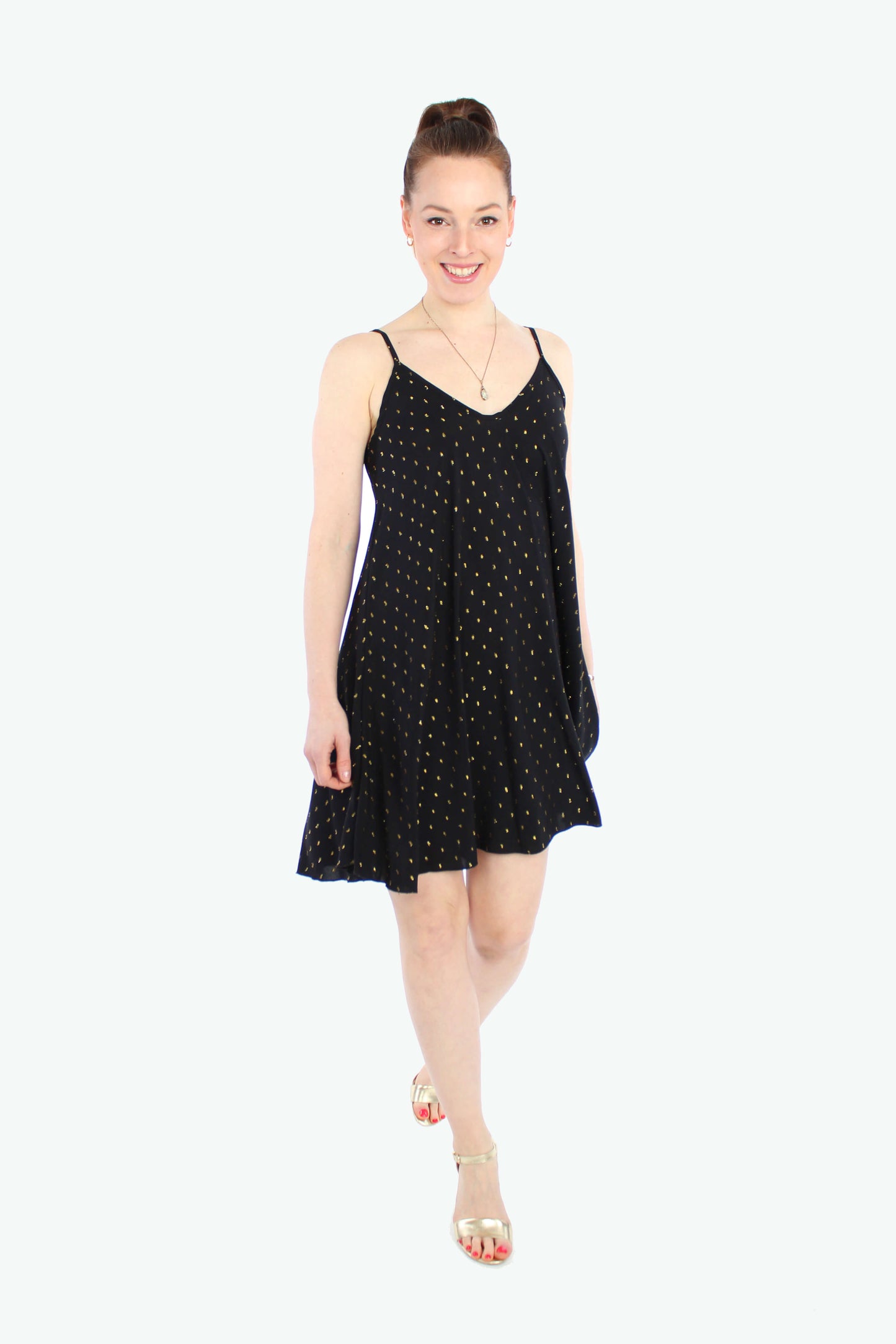 Frau, in einem lockeren Sommerkleid in Minilänge in schwarz mit goldenen Punkten. Das Trägerkleid besteht aus leichten Viskosestoff.