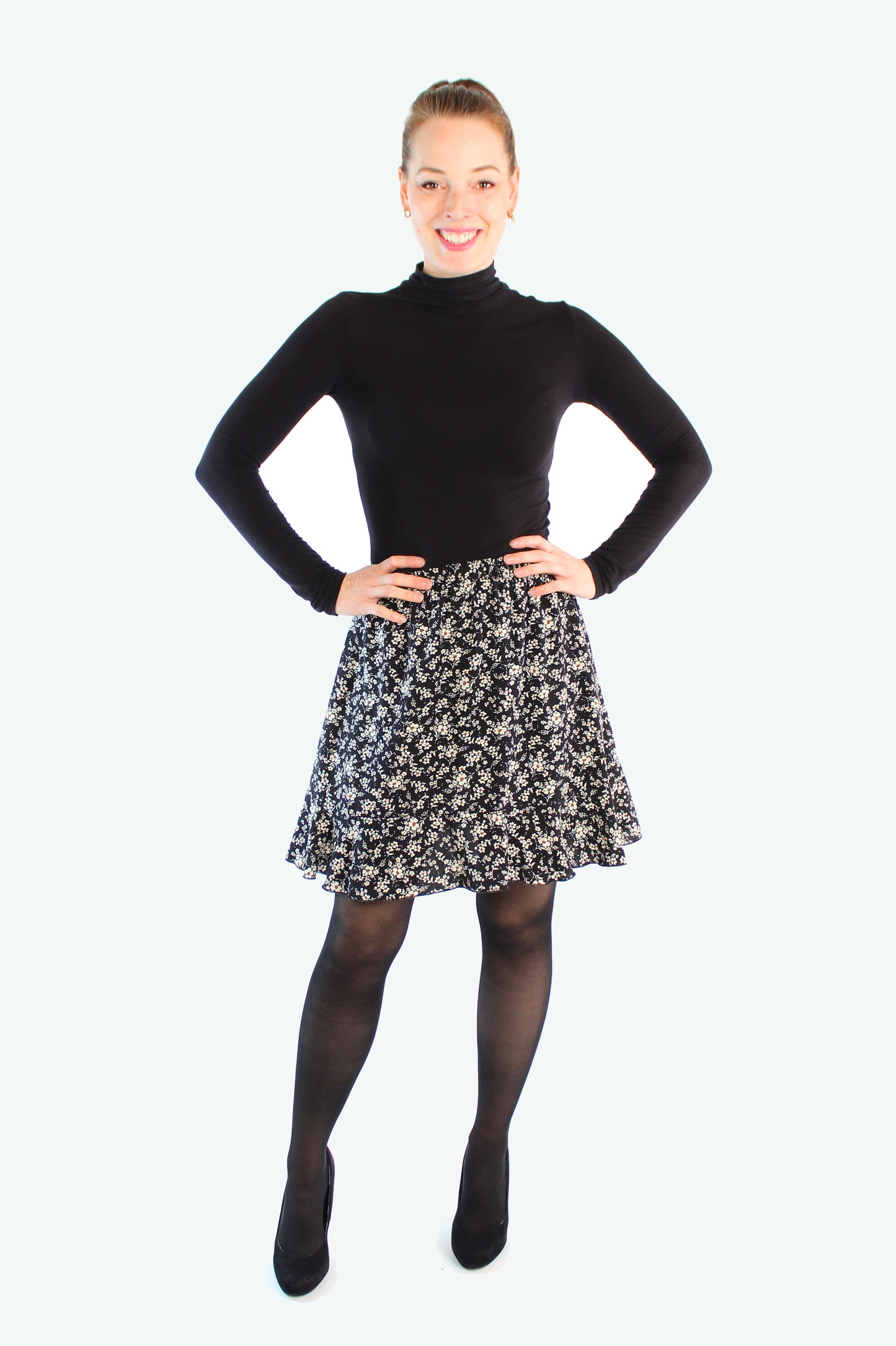 Model trägt Minirock in schwarz geblümt von LA.LUKA Berlin mit Volantsaum kombiniert mit einer schwarzen Strumpfhose – idealer Herbstrock für Damen.