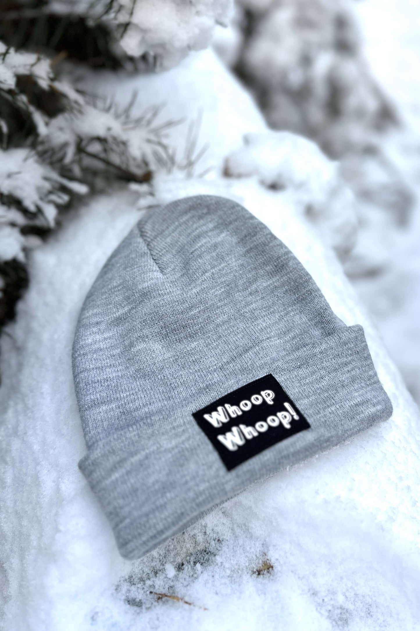 Graue Mütze mit Whoop Whoop! Motiv von LA.LUKA Berlin, liegt im Schnee.