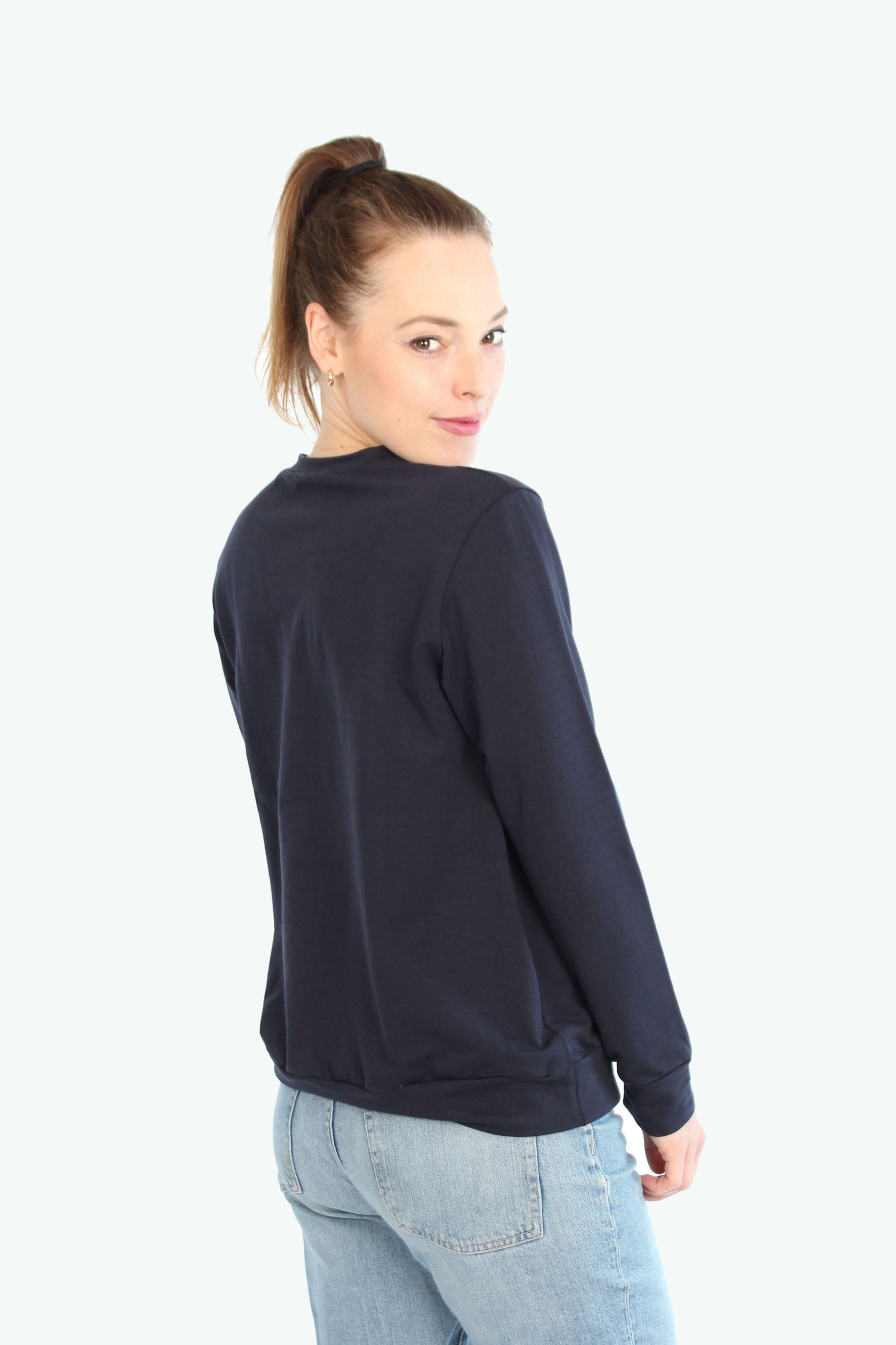 Frau schaut über die Schulter nach hinten, sie trägt einen dunkelblauen Pullover. 