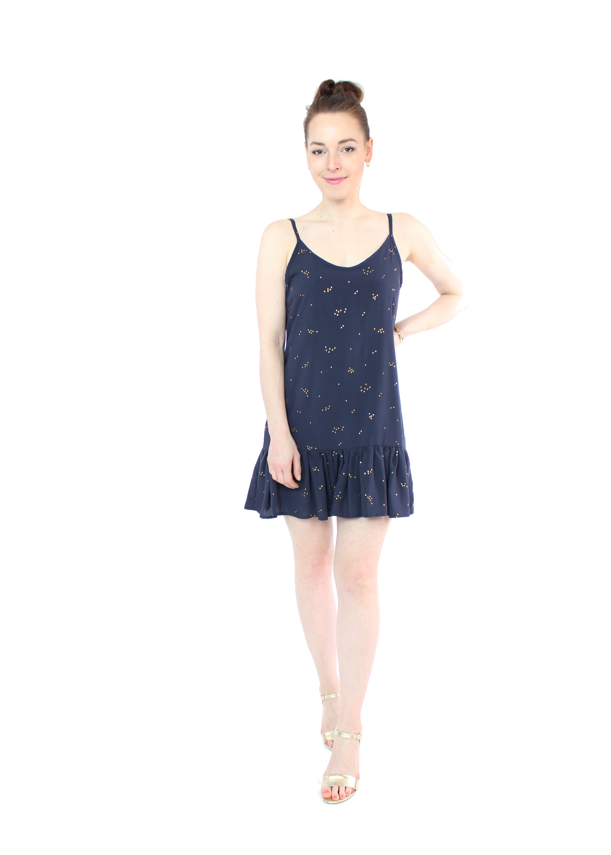 Model, in einem kurzen Trägerkleid in dunkelblau mit goldenen Punkten und Volants am Saum aus Viskose von LA.LUKA Berlin.