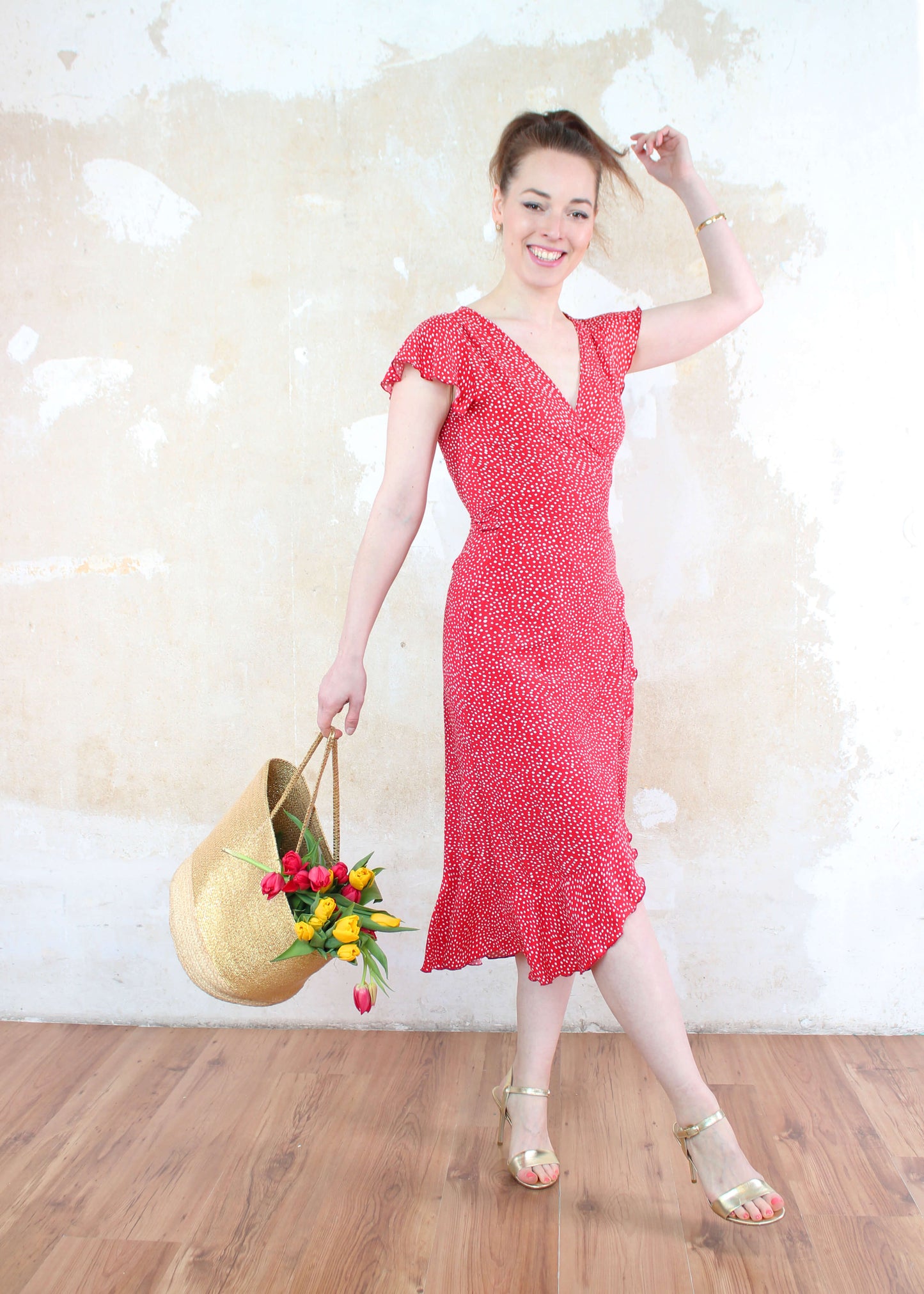 Model in einem langen Wickelkleid in rot mit weißen Punkten und kurzen Ärmeln aus leichtem Viskosestoff von LA.LUKA Berlin, mit einer Tasche mit Tulpen in der Hand.