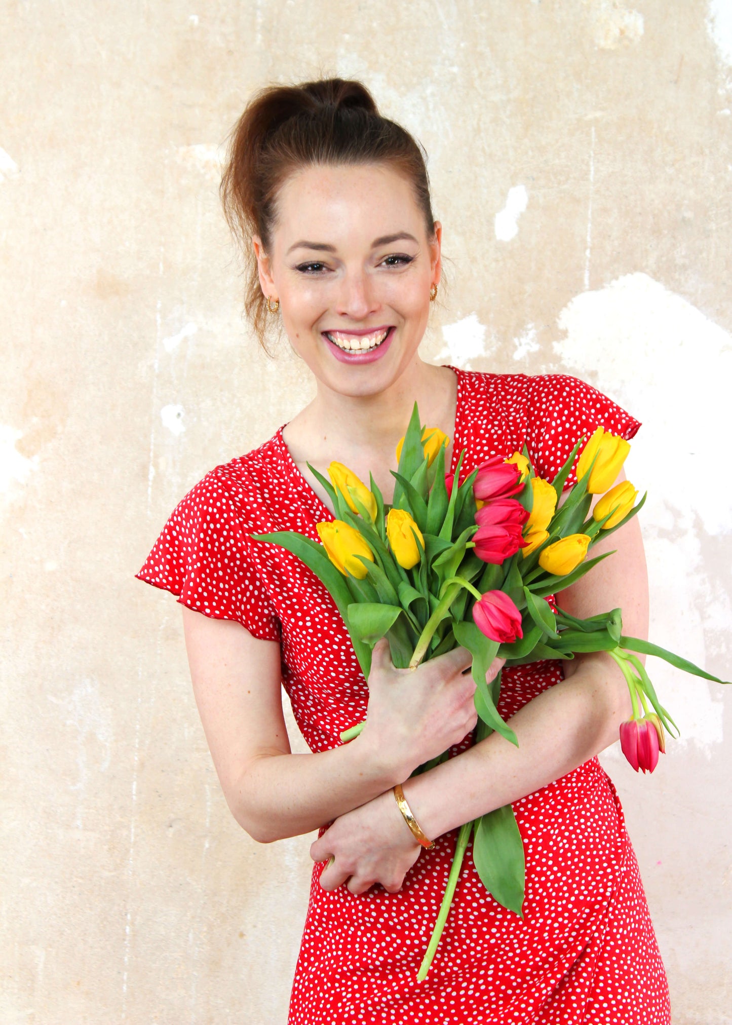 Frau in einem sommerlichen Wickelkleid in rot mit weißen Punkten und kurzen Ärmeln aus leichtem Viskosestoff von LA.LUKA Berlin, mit Tulpen in der Hand.