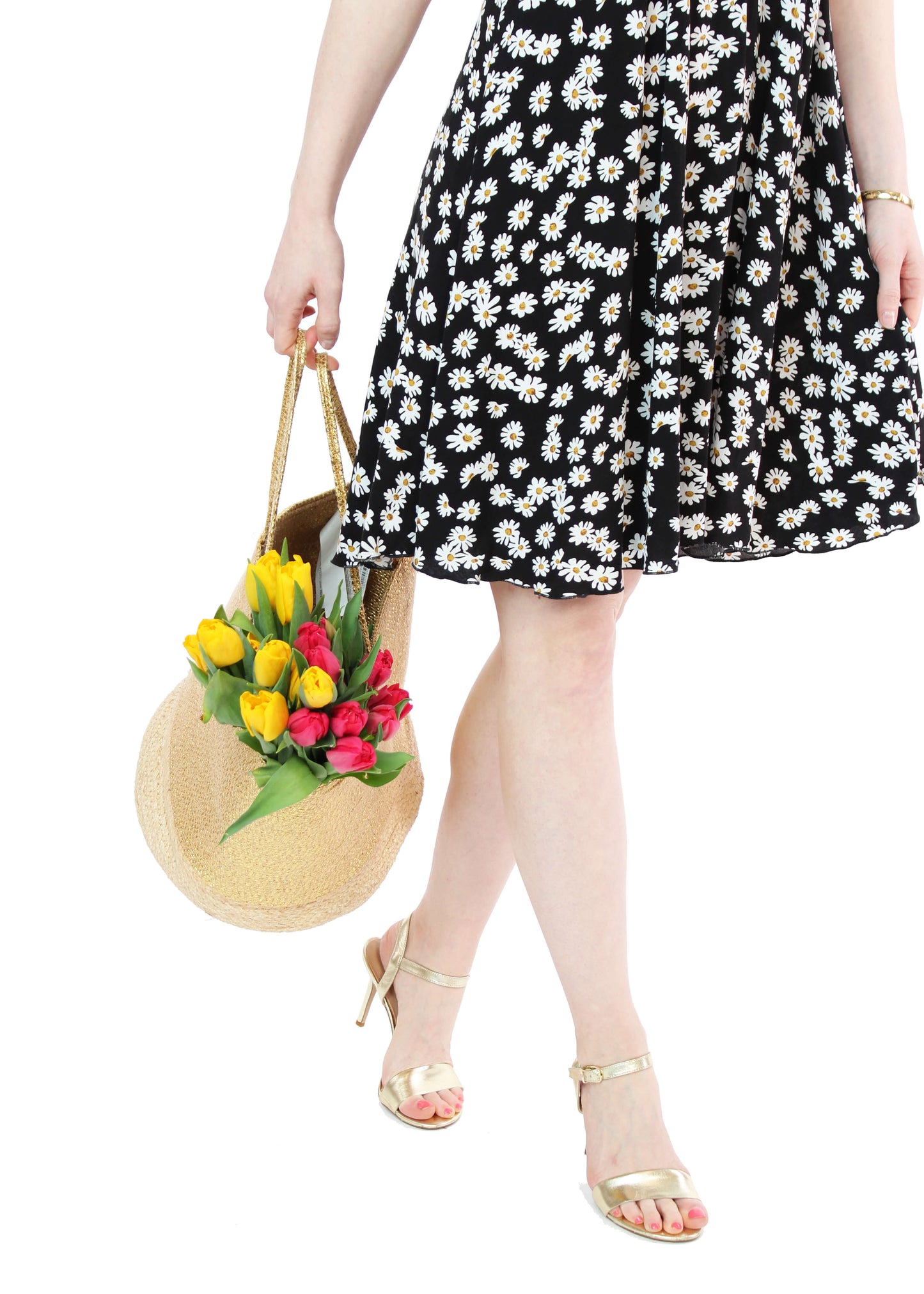 Frau in schwarzem Trägerkleid mit weißen Gänseblümchen von LA.LUKA Berlin trägt eine Strohtasche mit bunten Tulpen – perfektes Sommeroutfit 2025.