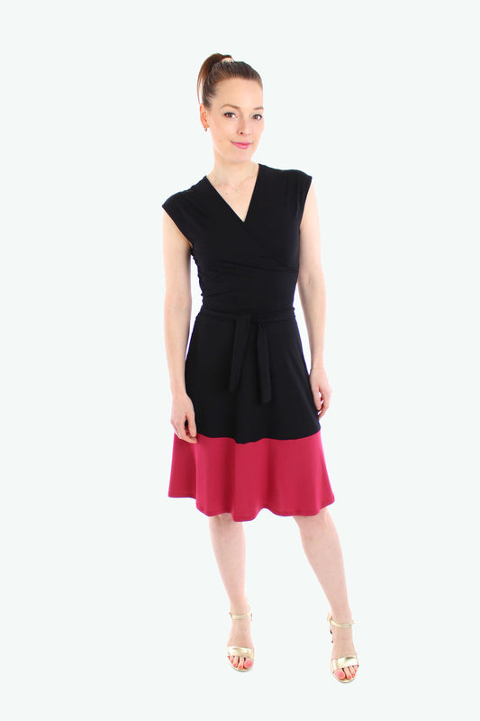 Frau trägt ein ärmelloses Jersey-Kleid mit schwarzem Oberteil und rotem Rockteil. Figurbetonter Schnitt mit V-Ausschnitt und Bindegürtel.
