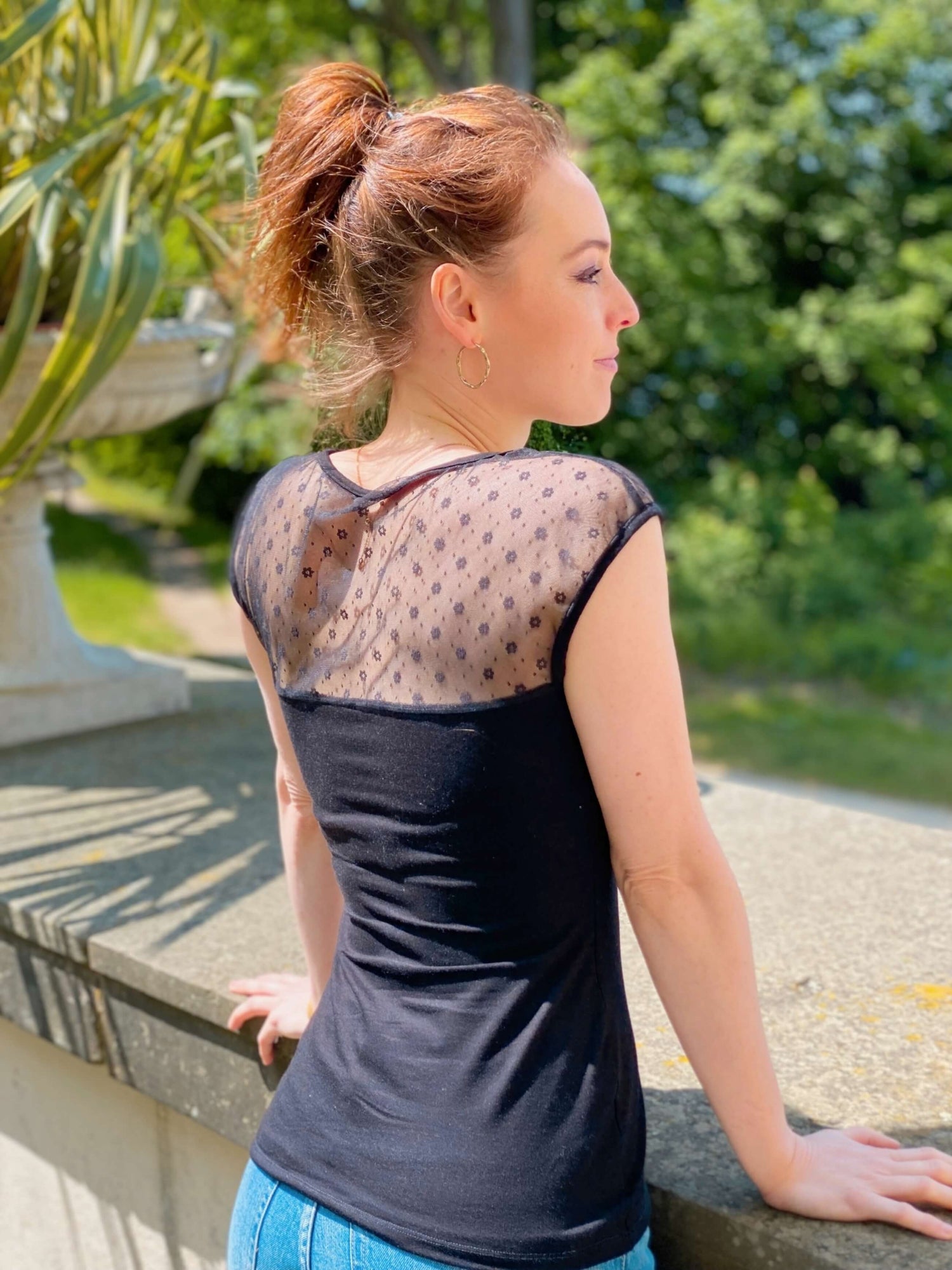 Frau in einem eleganten, engen Top in schwarz mit Blumentüll von LA.LUKA Berlin, schaut in die Ferne.