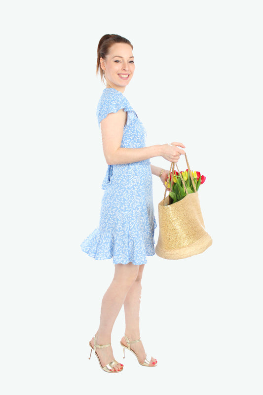 Model, in einem Sommerkleid in Minilänge zum wickeln in hellblau mit weißen Blümchenmuster aus leichtem Viskosestoff von LA.LUKA Berlin, trägt eine Korbtasche mit Tulpen. 