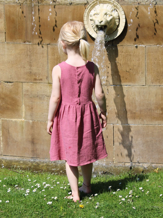 Kinderkleid in rosé mit goldenen Punkten aus Musselin von LA.LUKA Berlinauf einer Blumenwiese.