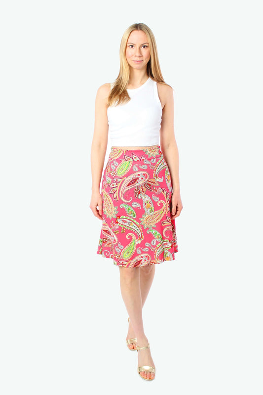 Model trägt knieumspielenden Sommerrock in A-Linie mit pinkem Paisley-Muster aus Jersey, kombiniert mit weißem ärmellosem Top und goldenen Sandalen, frontale Studioaufnahme vor hellem Hintergrund.