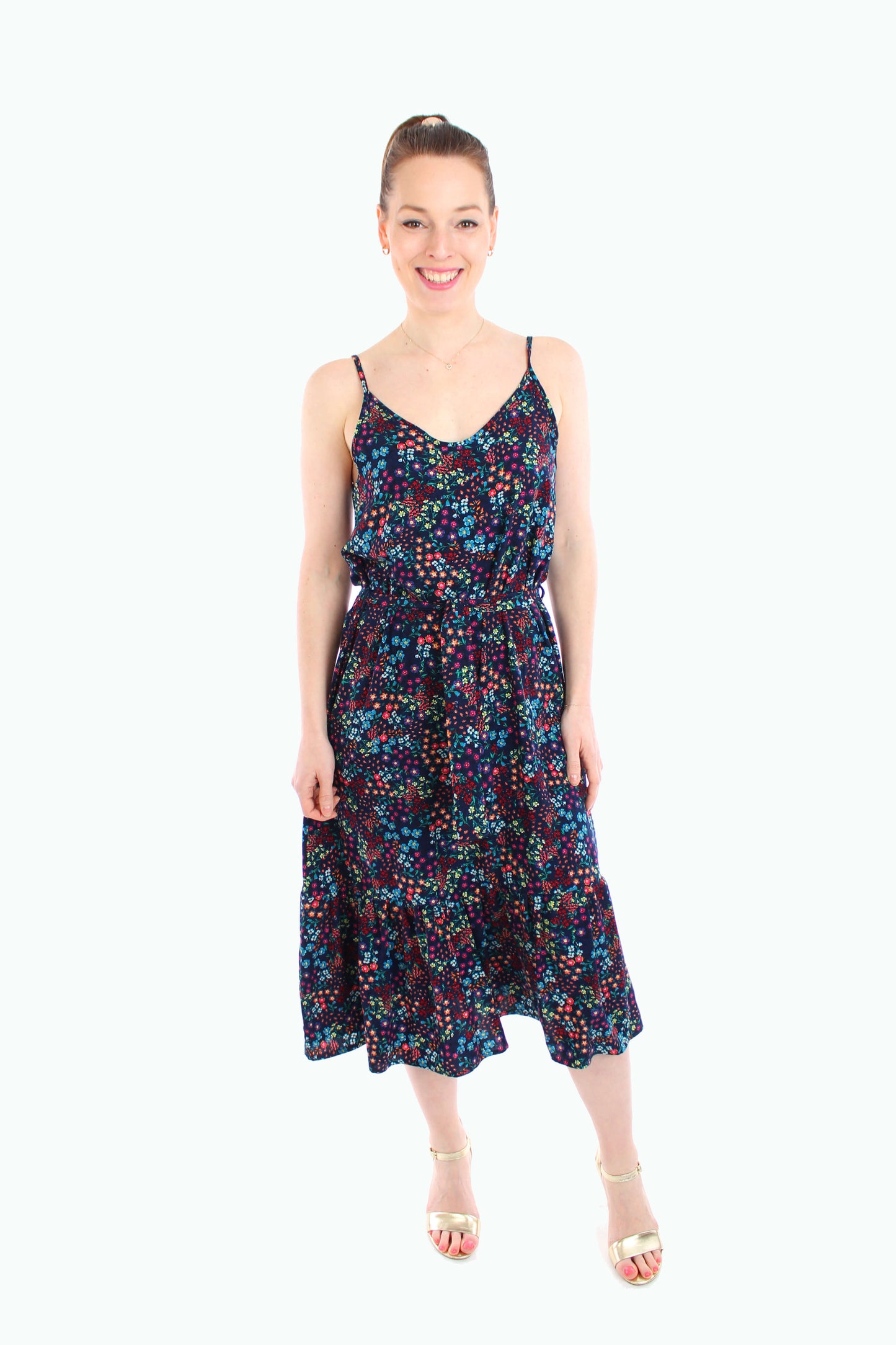 Frau trägt ein dunkelblaues, geblümtes Midikleid mit Spaghettiträgern und goldenen Highheels, perfekt für den Sommer.