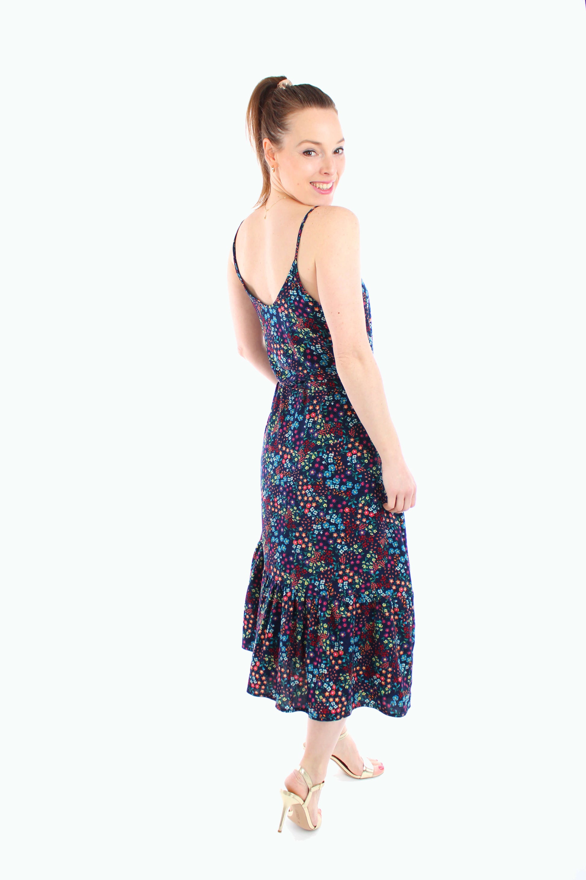 Rückansicht eines dunkelblauen, geblümten Midikleids mit Spaghettiträgern und Volant-Saum, getragen mit goldenen High Heels – feminin, luftig und perfekt für den Sommer.