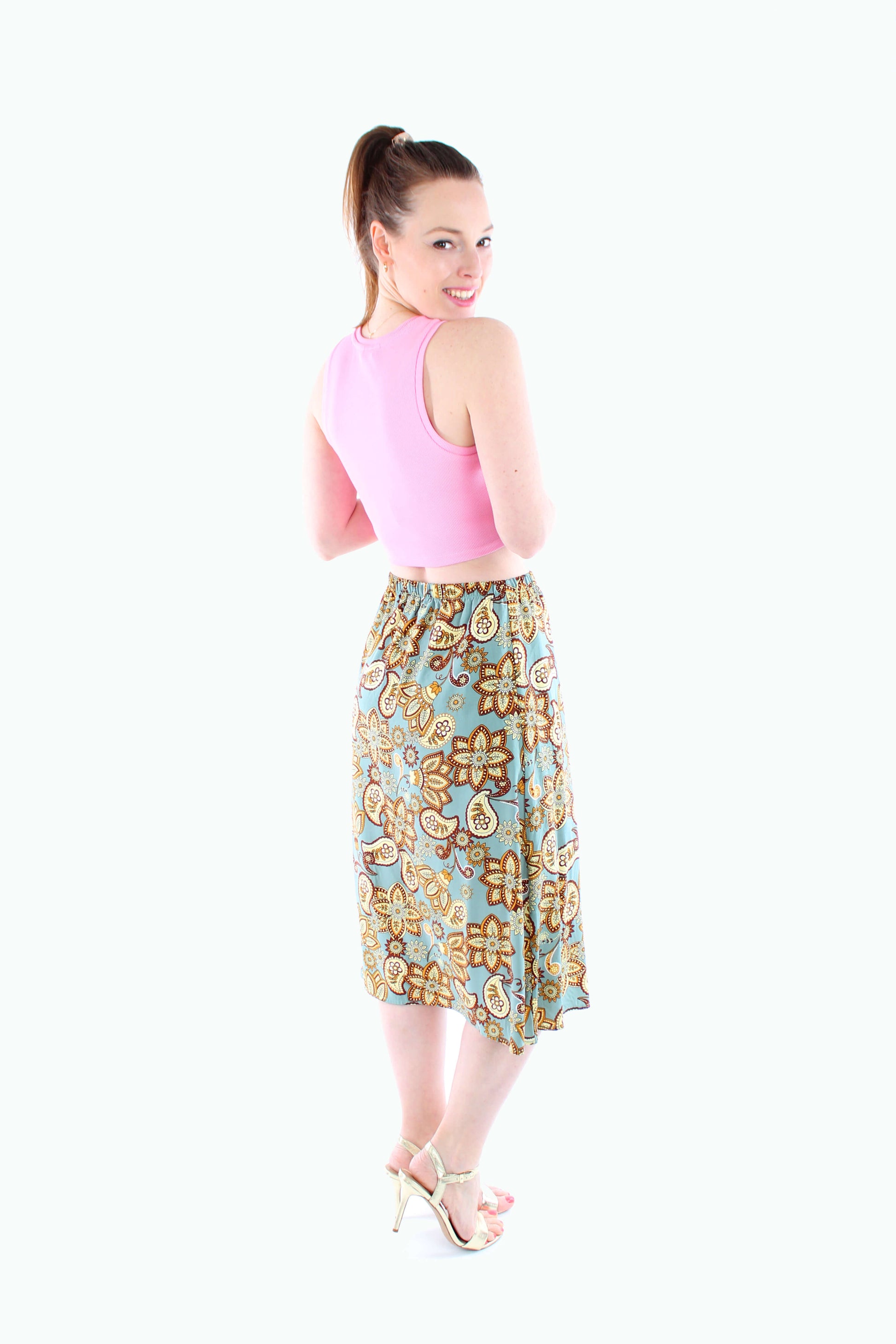 Rückansicht eines mintfarbenen Damen-Midirocks mit auffälligem Paisley-Muster in Braun- und Gelbtönen – kombiniert mit einem rosa Croptop für einen sommerlichen Look.