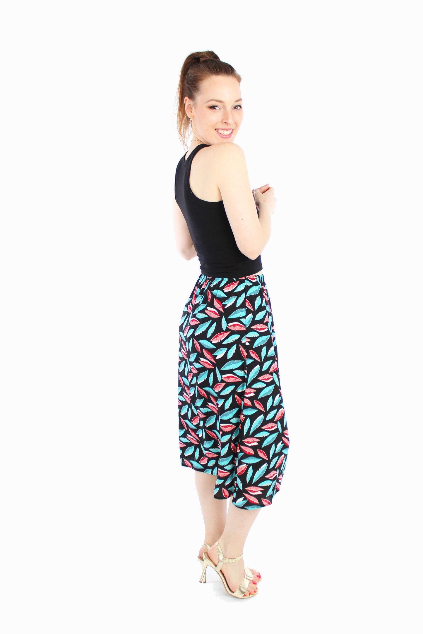 Model trägt schwarzen Midirock mit buntem Blättermuster und elastischem Bund kombiniert mit einem schwarzem Top in der Rückansicht.