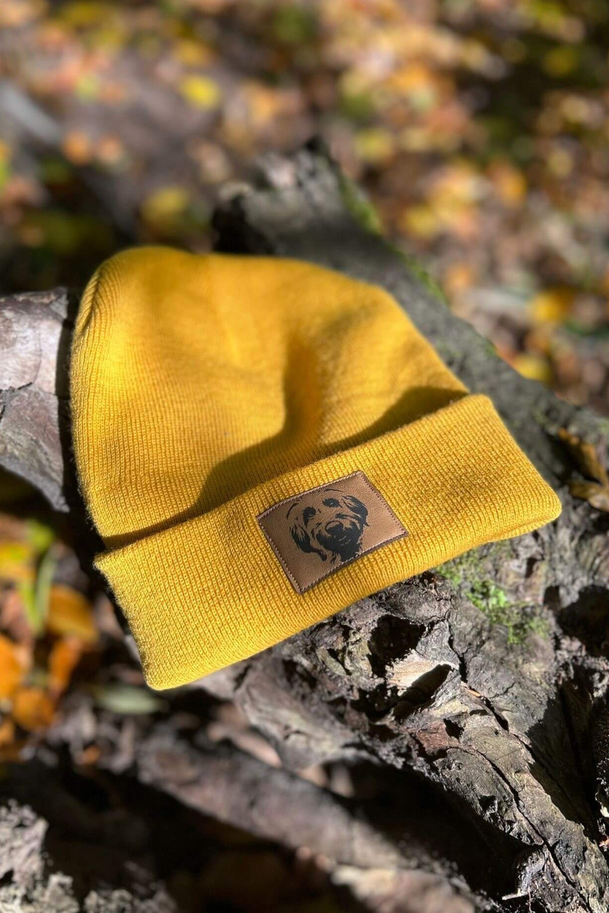Senfgelbe Mütze von LA.LUKA Berlin mit braunem Kunstleder-Patch und Labradoodle-Motiv, fotografiert im herbstlichen Waldlicht – modisches Accessoire für Hundefreunde.
