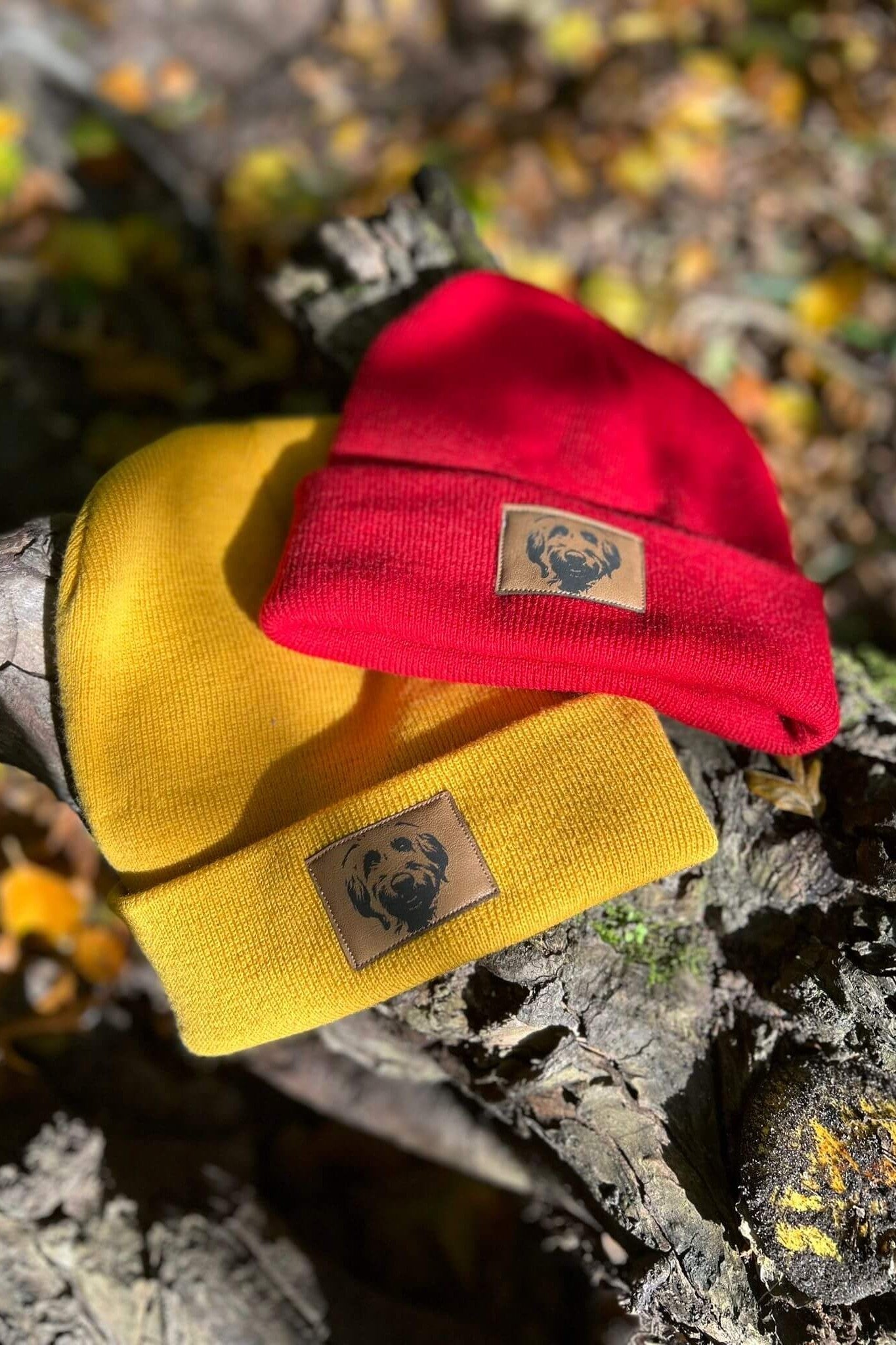 Zwei Mützen in Senfgelb und Rot von LA.LUKA Berlin, jeweils mit braunem Kunstleder-Patch und Labradoodle-Motiv – stilvolle Beanies für Hundeliebhaber, ideale Geschenkidee.