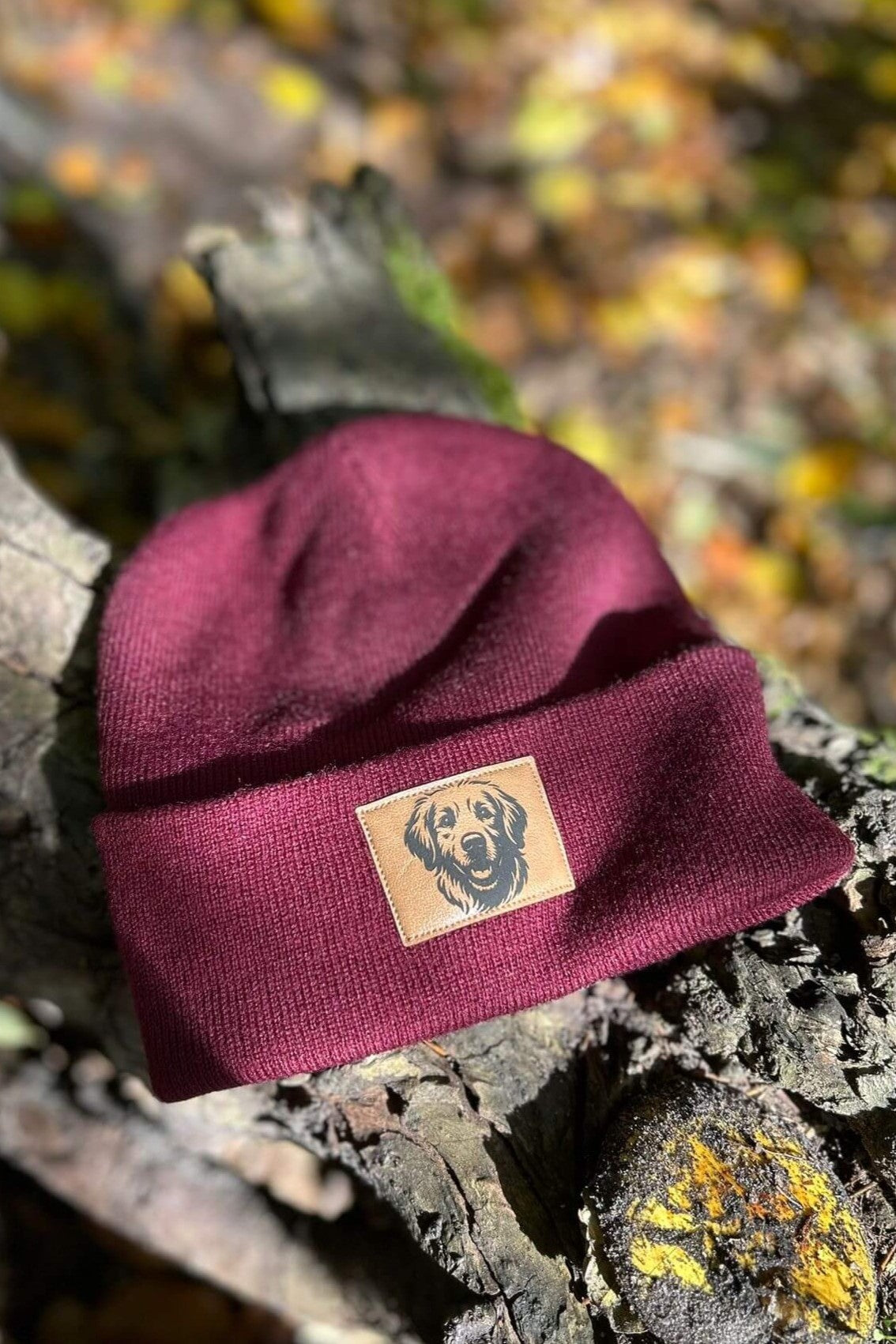 Bordeauxrote Mütze von LA.LUKA Berlin mit braunem Kunstleder-Patch und Labrador-Motiv, stilvoll auf Baumrinde im Sonnenlicht arrangiert – hochwertige Beanie und liebevolles Geschenk für Hundefreunde.