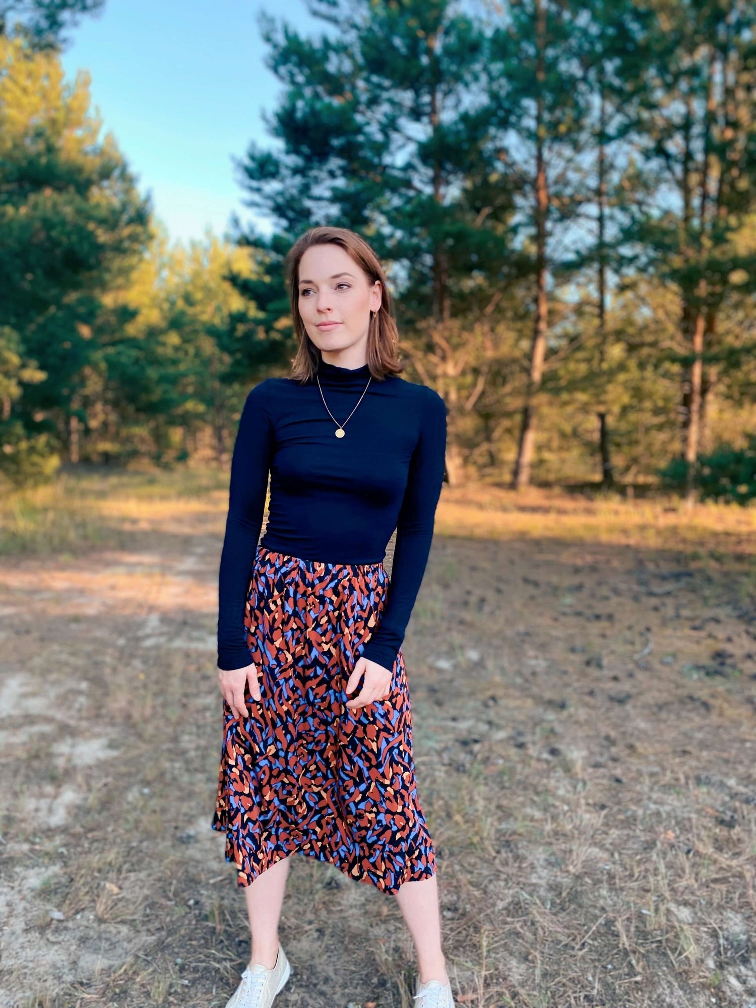 Frau in einem schwarzen Midirock mit Brauntönen von LA.LUKA Berlin, im Hintergrund ein Wald. 