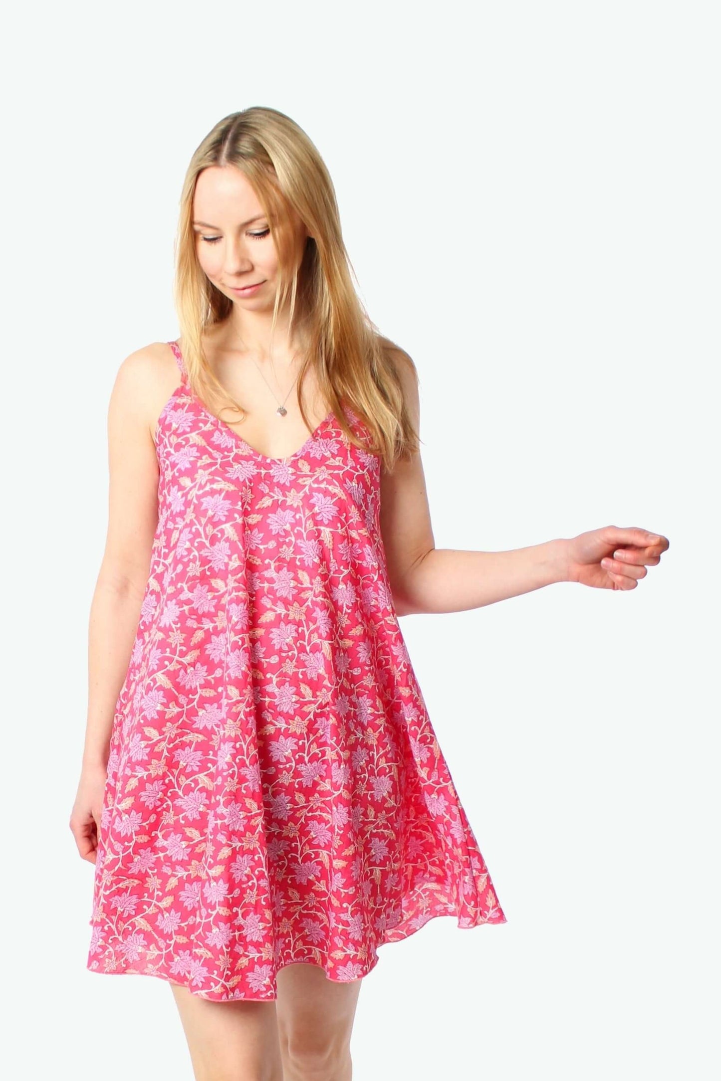 Model trägt ein pink geblümtes Trägerkleid in A-Linie mit feinem Blumenmuster, fließendem Stoff und V-Ausschnitt, leichte Bewegung des Saums, Studioaufnahme vor weißem Hintergrund.