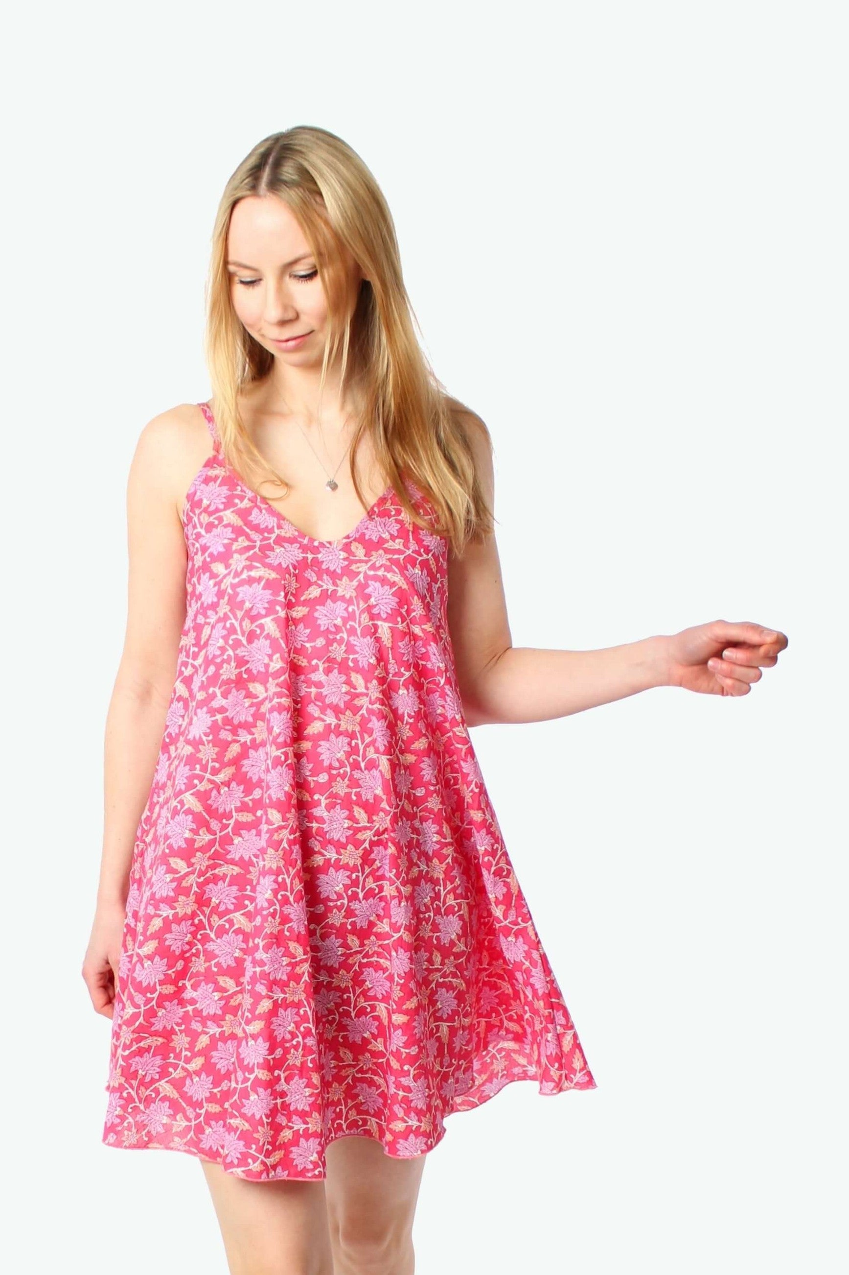 Model trägt ein pink geblümtes Trägerkleid in A-Linie mit feinem Blumenmuster, fließendem Stoff und V-Ausschnitt, leichte Bewegung des Saums, Studioaufnahme vor weißem Hintergrund.