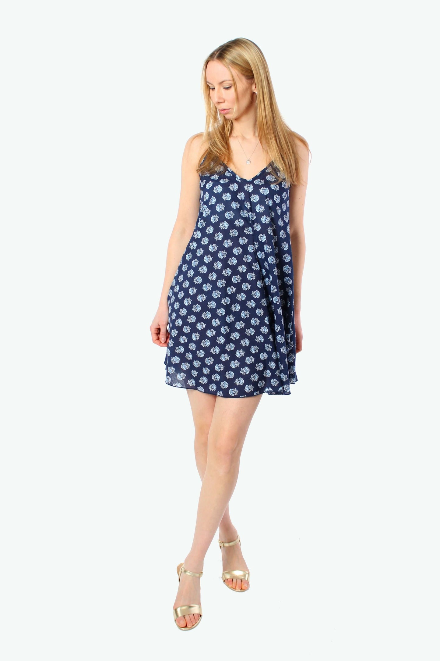 Model trägt luftiges dunkelblaues Sommerkleid mit Spaghettiträgern und hellem floralem Muster, locker geschnittenes kurzes Trägerkleid aus leichtem Stoff.